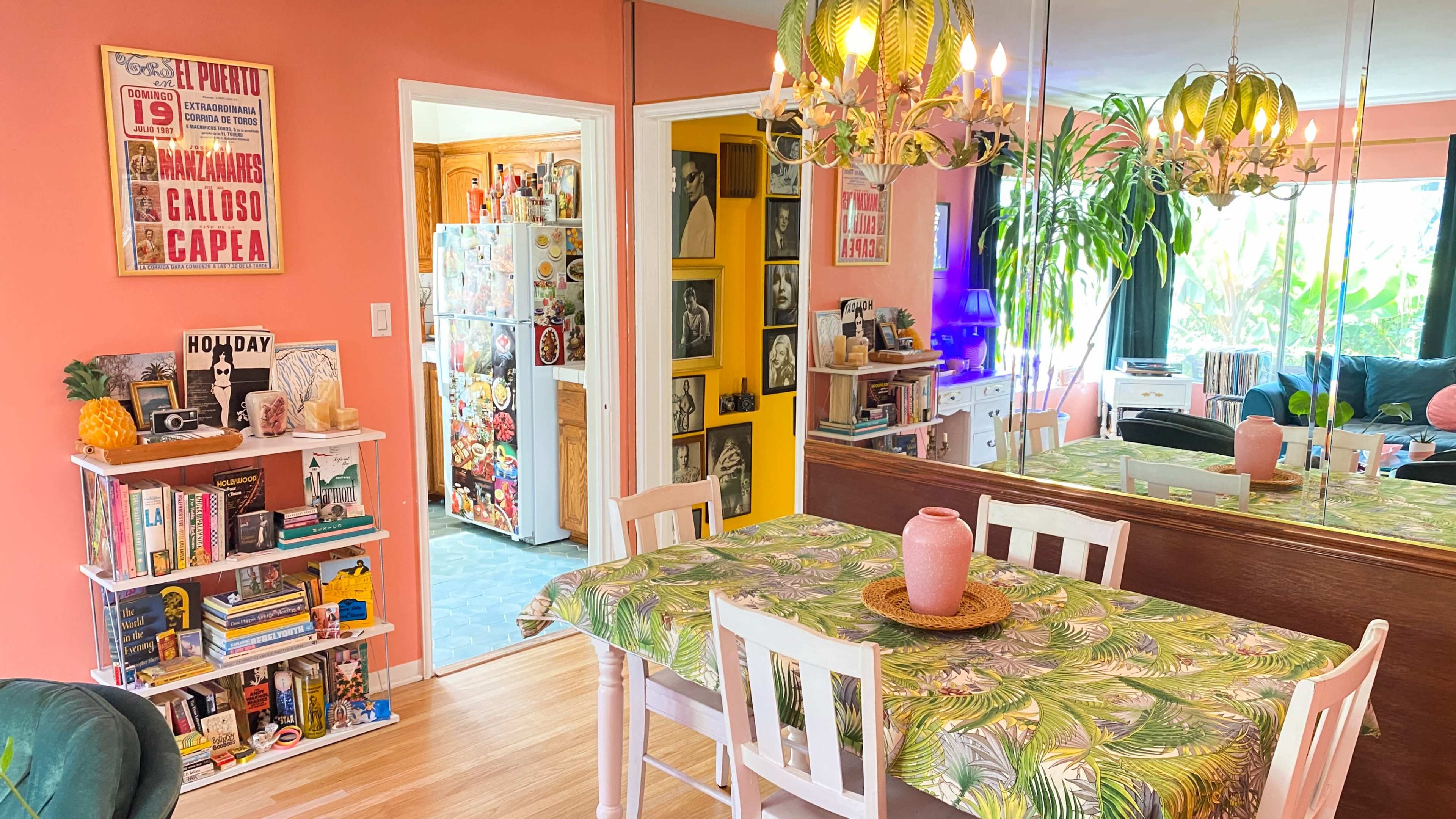 A bright dining area features a tropical-patterned tablecloth, a pink vase centerpiece, and colorful decor against pastel walls.