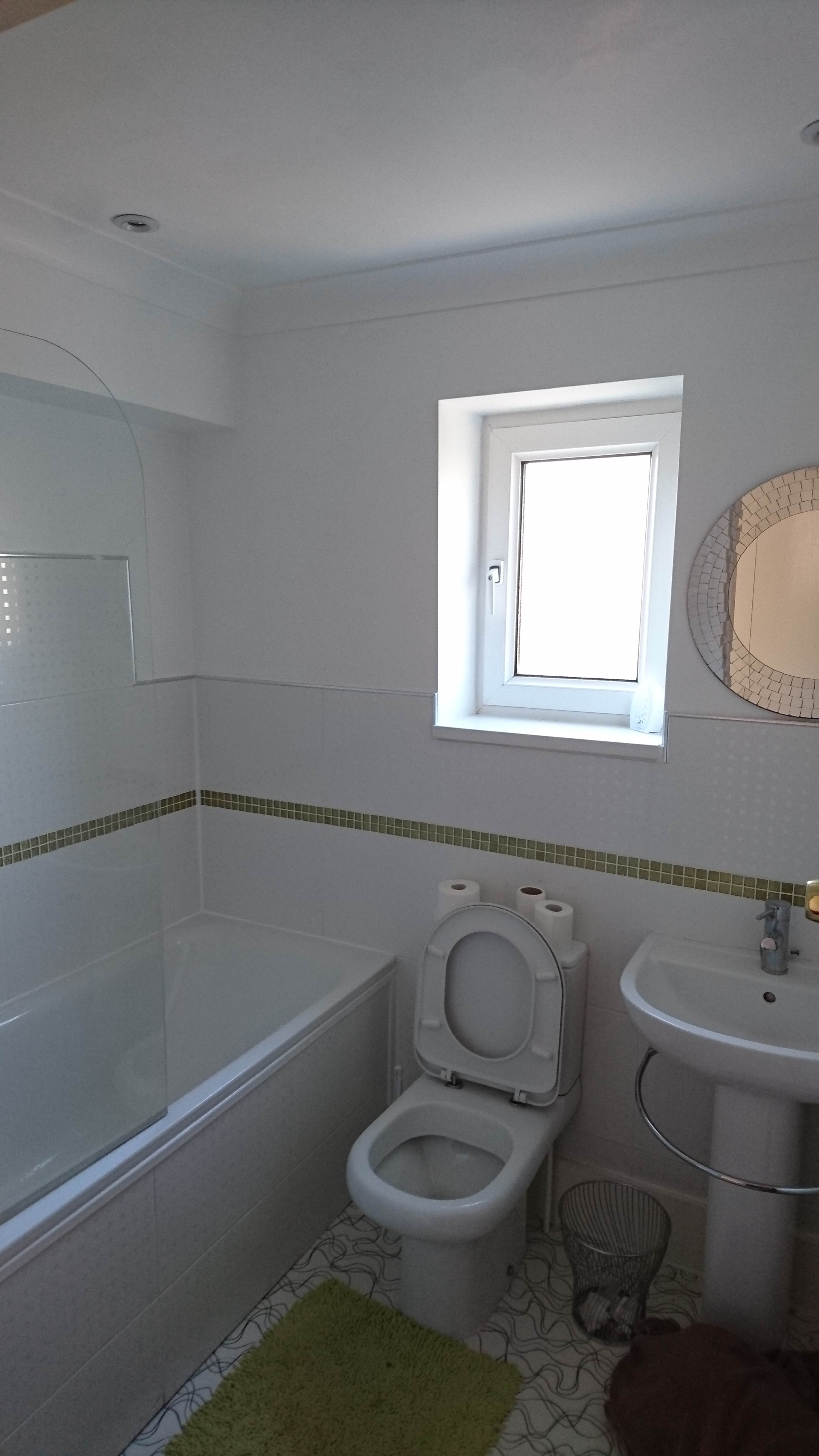 The image shows a bathroom featuring a bathtub, toilet, sink, and a small window.