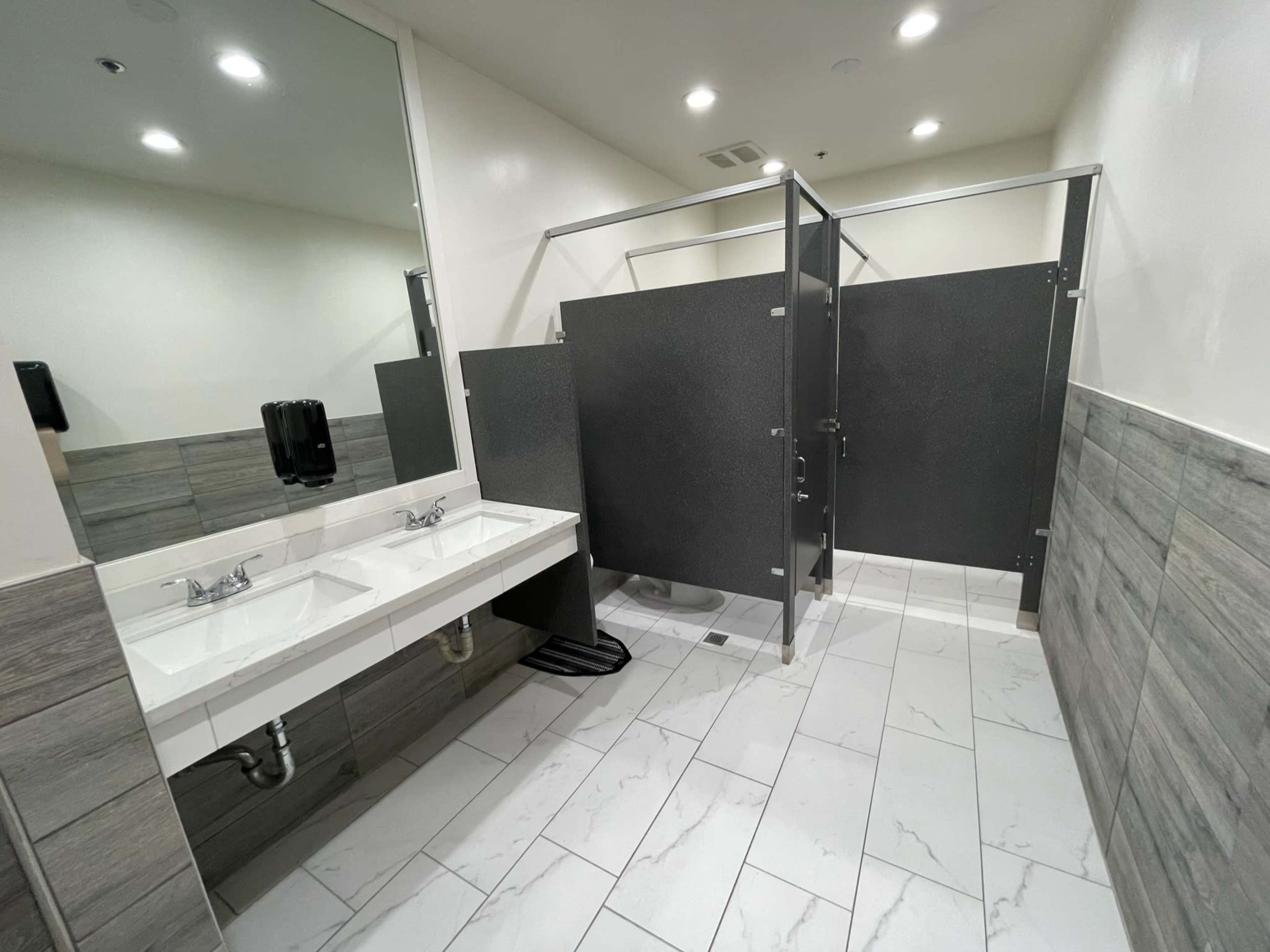 A clean restroom with two sink basins and a partitioned toilet area.