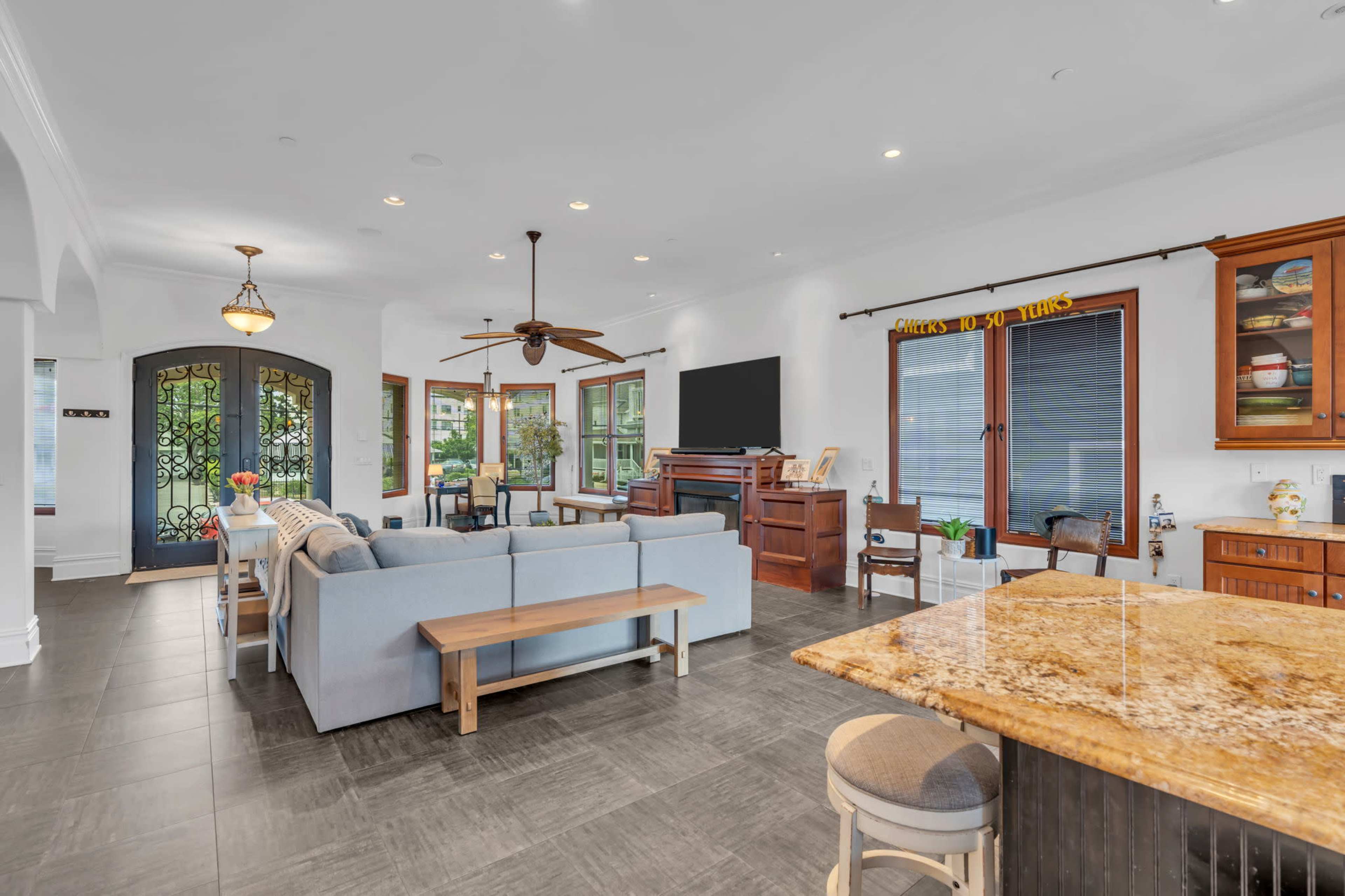 The image shows a modern living space featuring an open layout with a seating area, a large window, and a kitchen bar topped with granite.