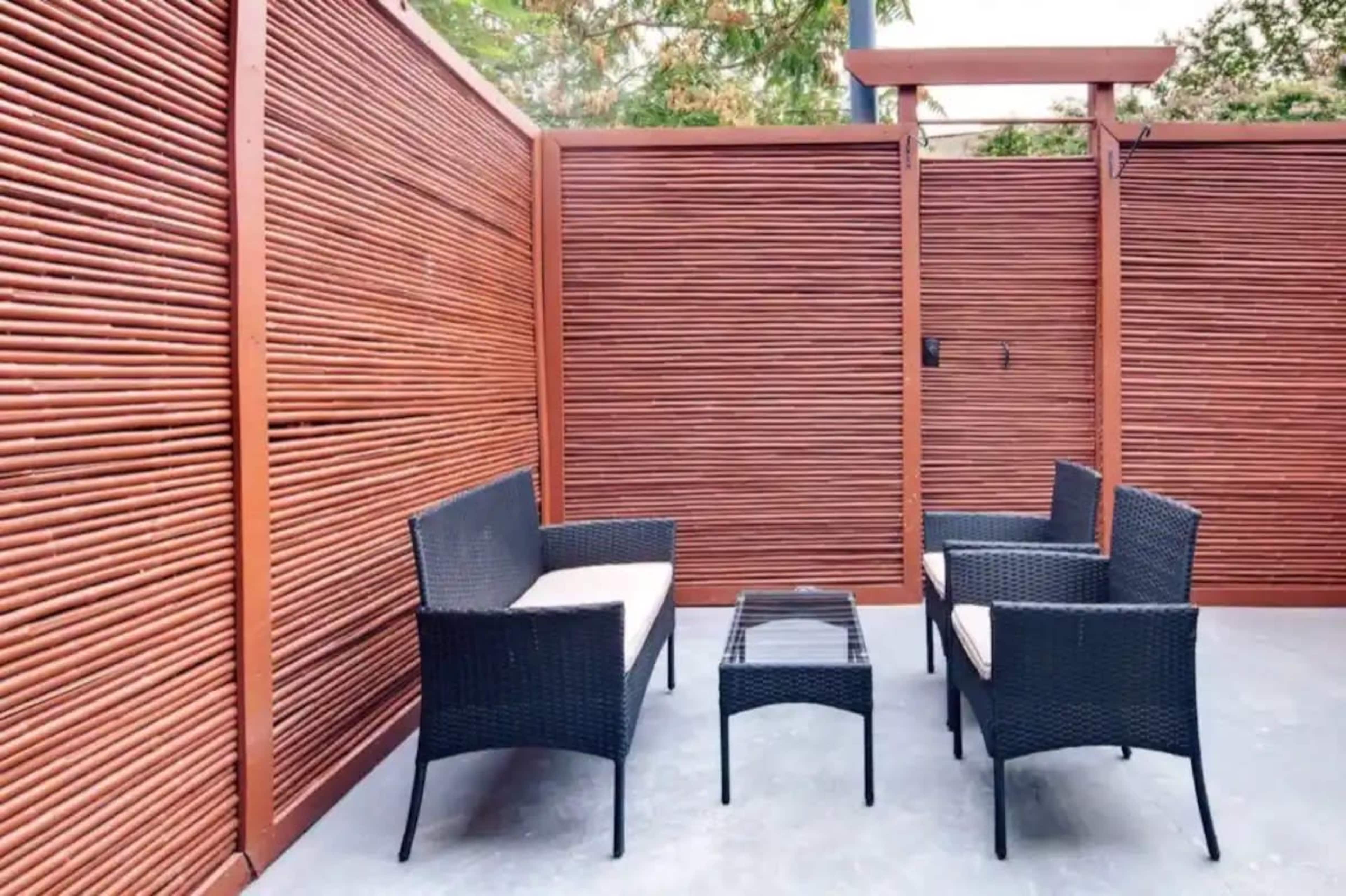 A patio area with a set of four black wicker chairs and a glass-top coffee table, surrounded by wooden slat walls.