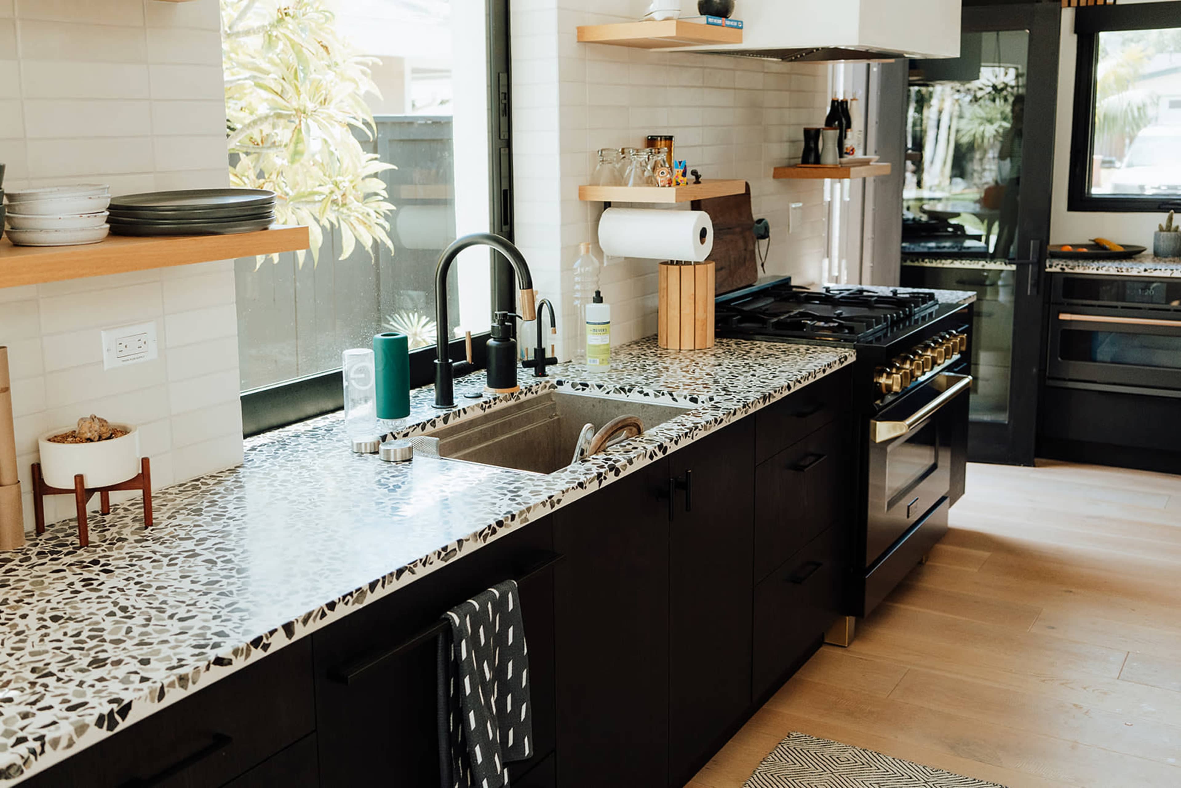 The image shows a modern kitchen featuring a dark cabinetry, a spacious sink with a patterned countertop, and a gas range beside a window.