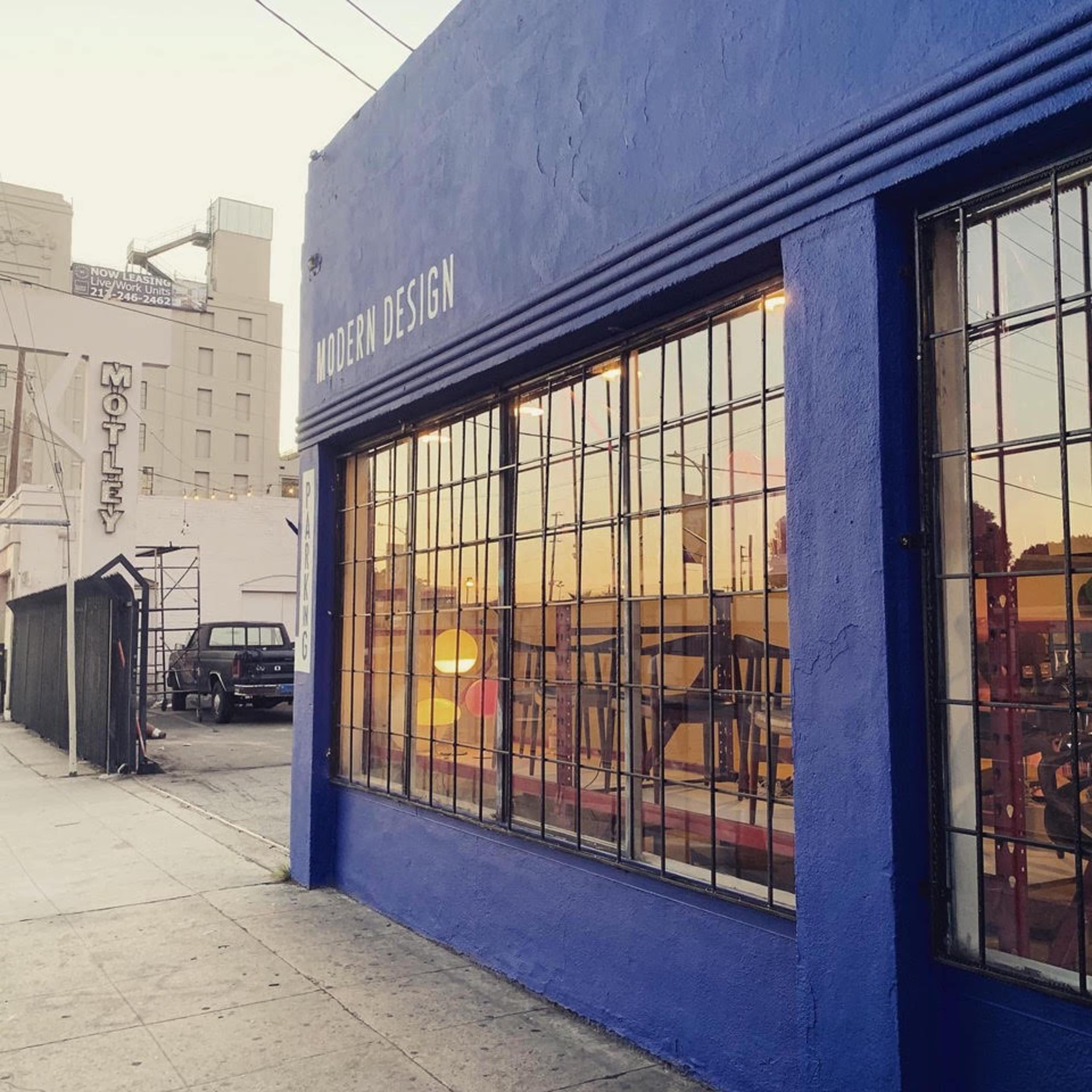 A blue building with large windows displaying reflections and a sign that reads "MODERN DESIGN" on a street with a parked black vehicle.