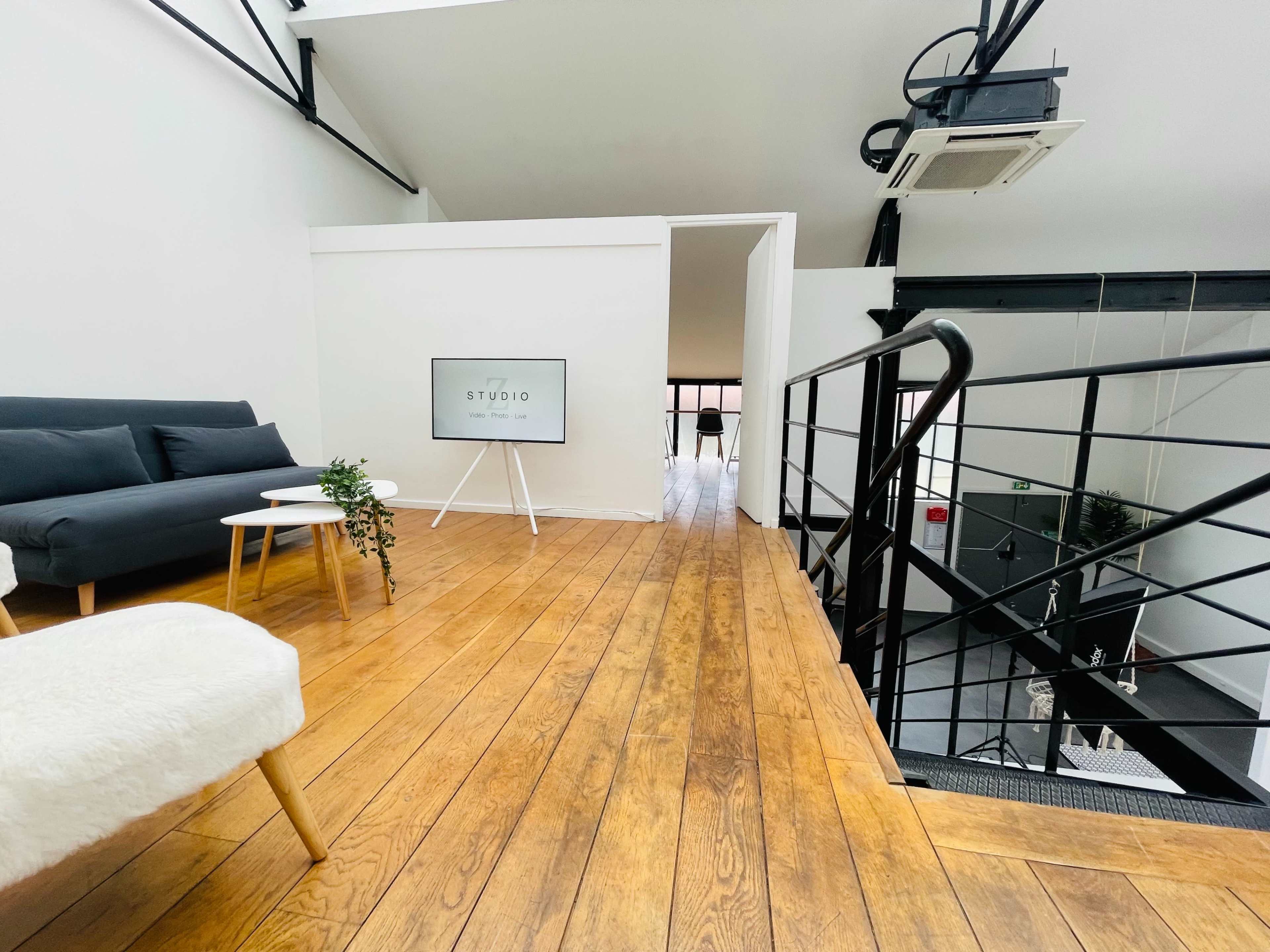 A modern, open space with wooden floors, a black sofa, a small table, and a sign that reads "STUDIO" on an easel.