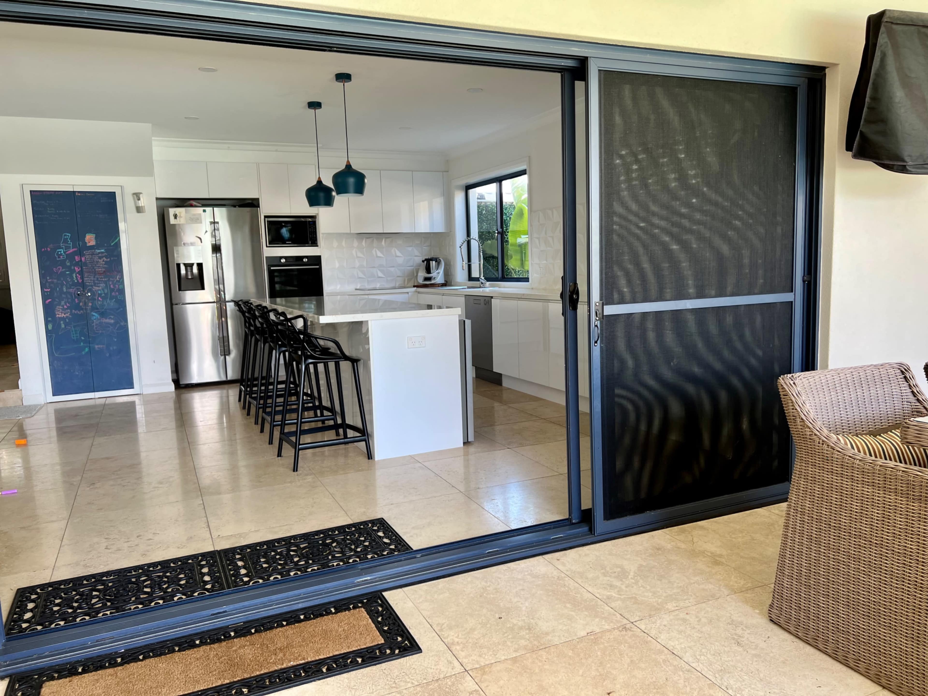 The image shows a modern kitchen with white cabinets, stainless steel appliances, and a sliding glass door leading to an outdoor seating area.