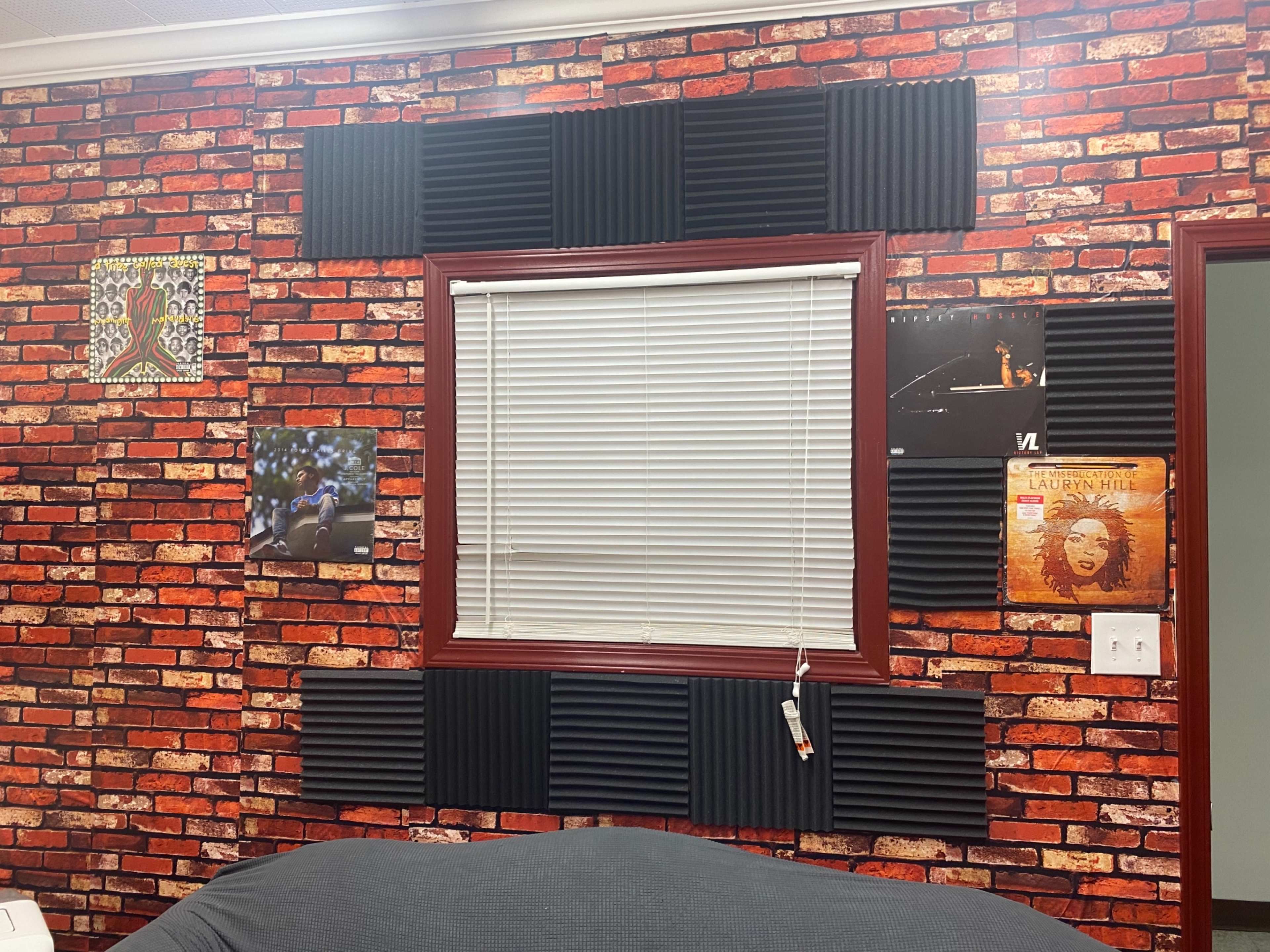 A window framed by a red brick-patterned wall with soundproofing panels arranged around it, alongside various framed artworks and posters.