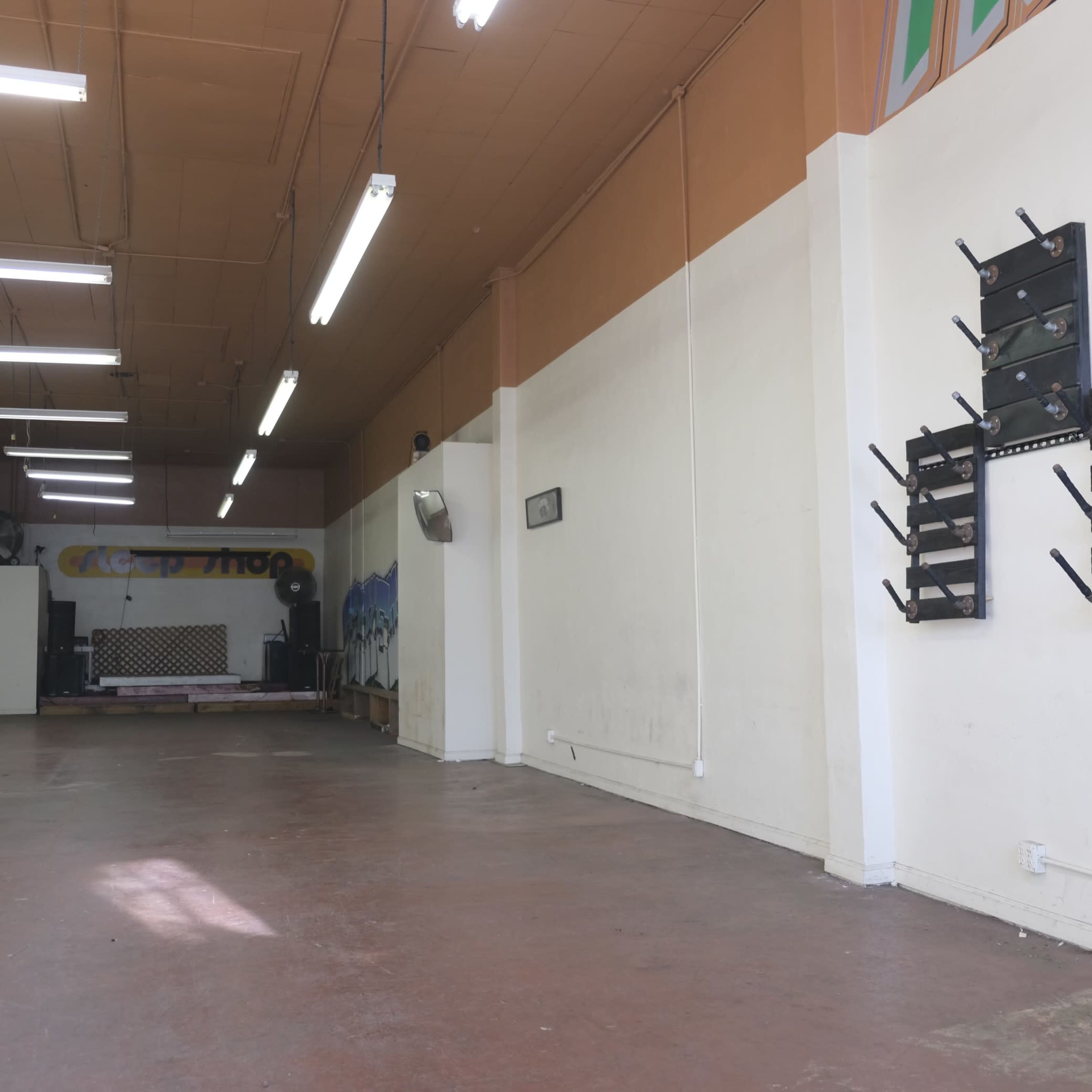 The image shows a spacious, empty room with a polished concrete floor, bright overhead lights, and a stage area at the far end.