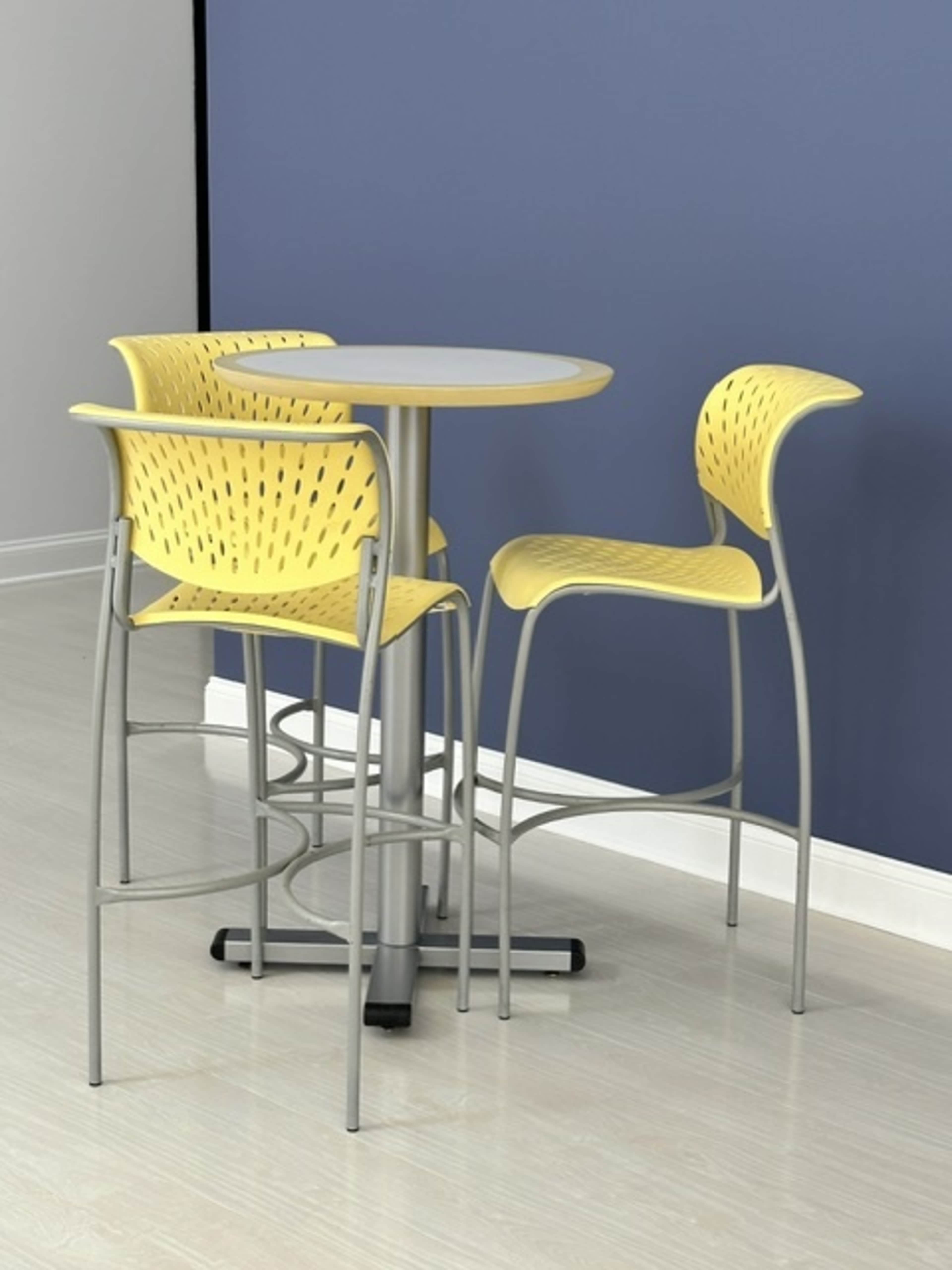 A small round table with three yellow high-back chairs is situated against a blue wall.