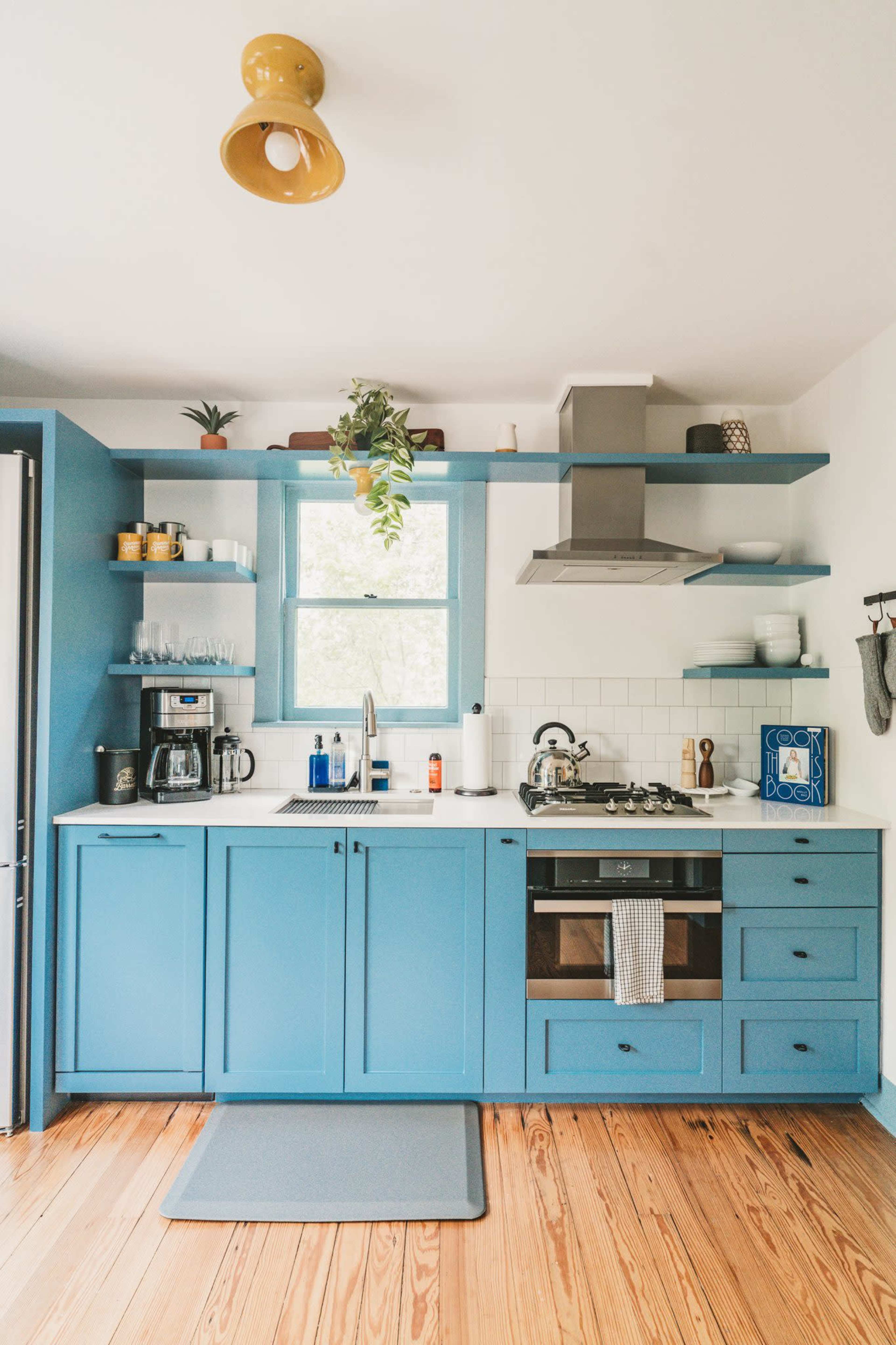 A modern kitchen features blue cabinetry, a white countertop, a gas stove, and various appliances arranged neatly.