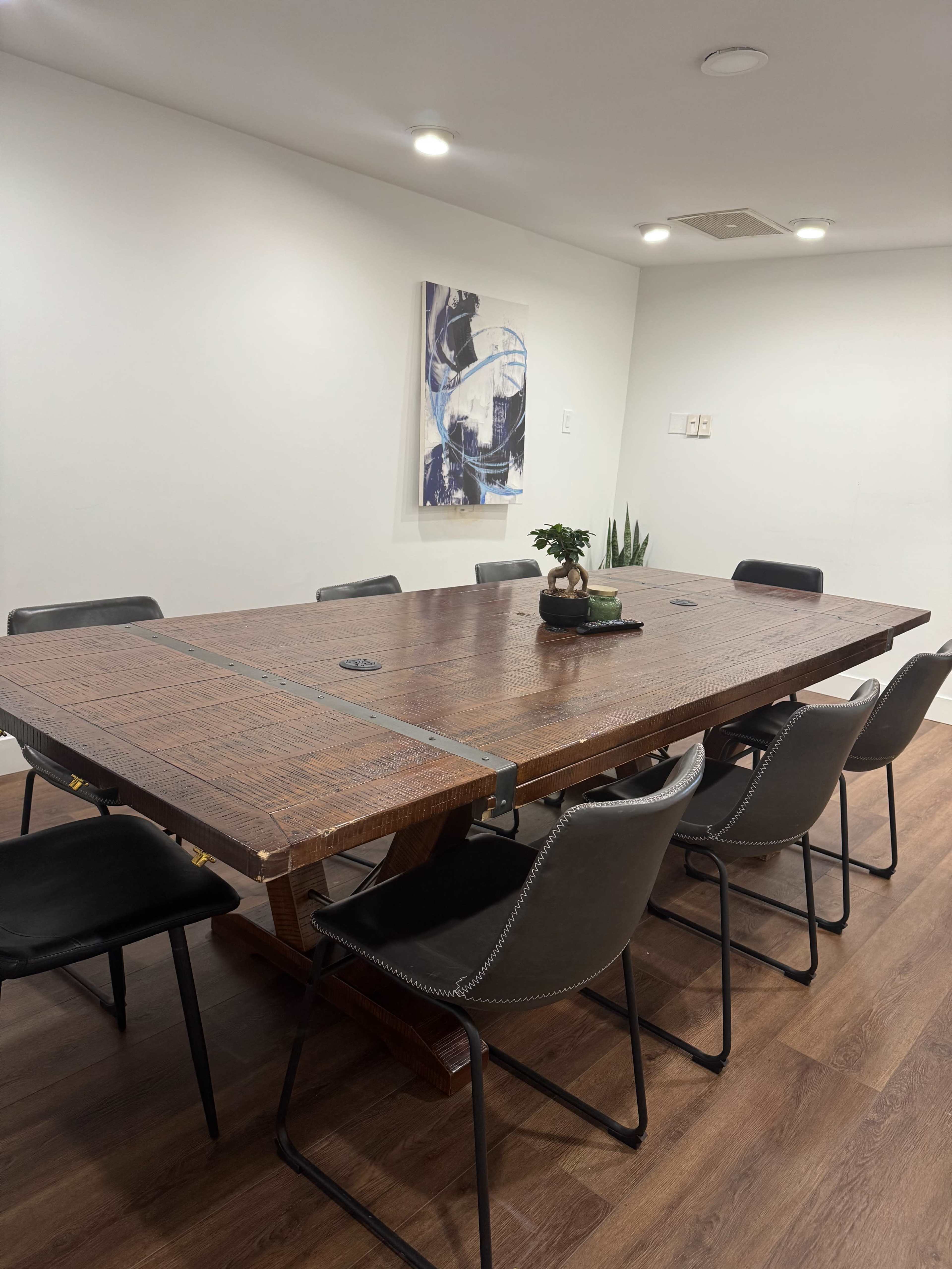 The image shows a large wooden conference table surrounded by black chairs in a well-lit meeting room.