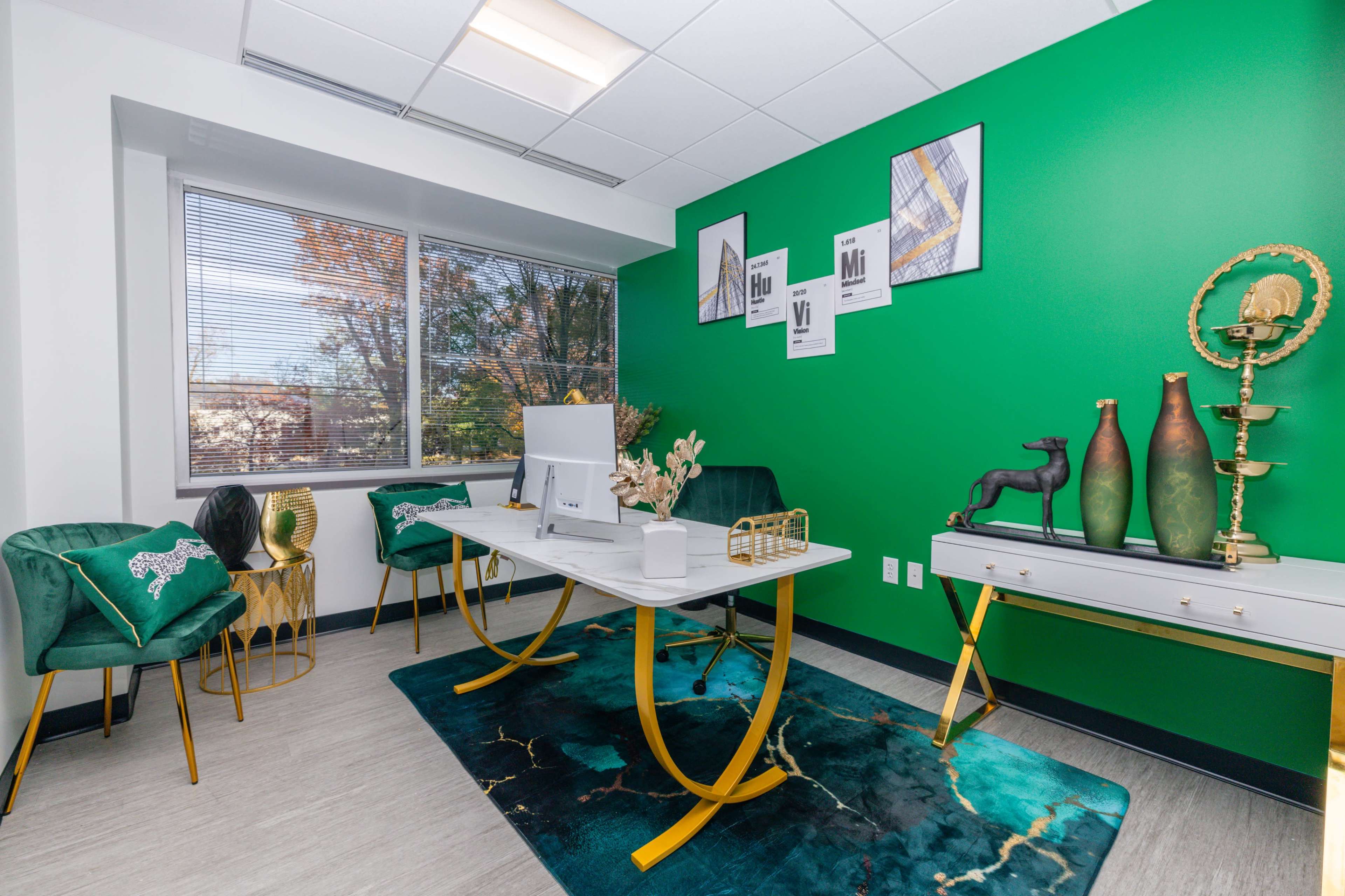 A modern office with a green accent wall, a white desk in the center, and decorative items including a rug, vases, and framed artwork.