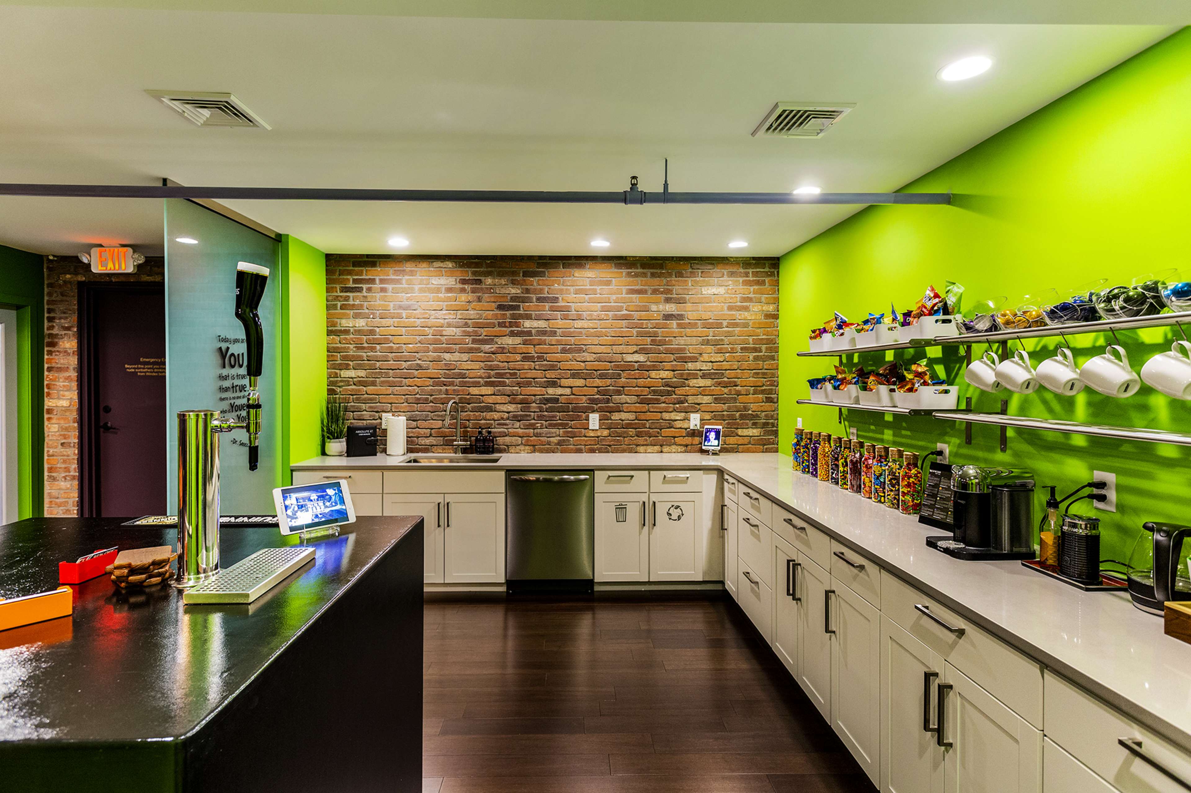 A modern kitchen with a green accent wall, brick backsplash, and white cabinetry, featuring a variety of kitchen appliances and colorful items on display.
