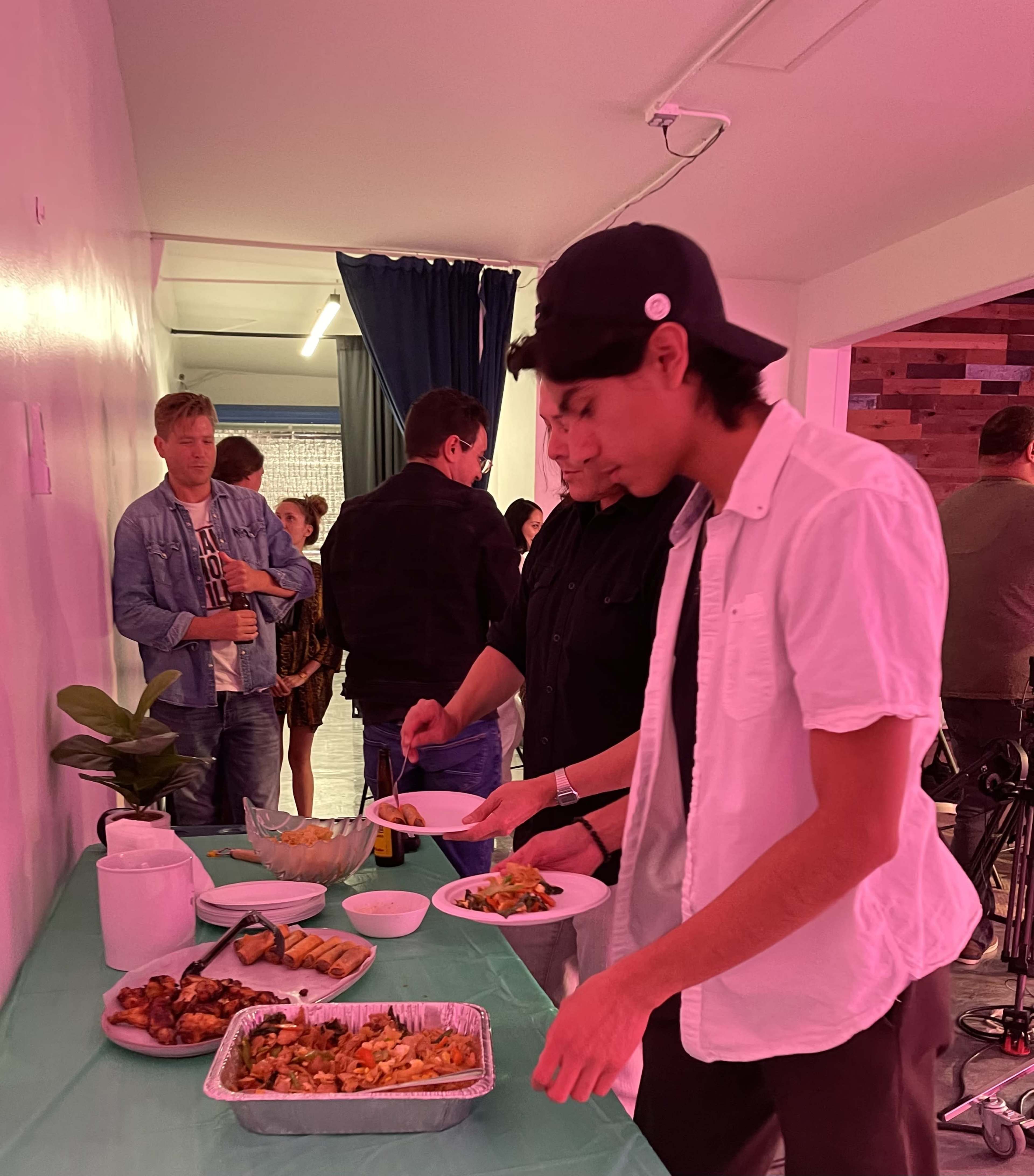 A group of people is gathered at a table serving food, while two individuals are filling their plates.