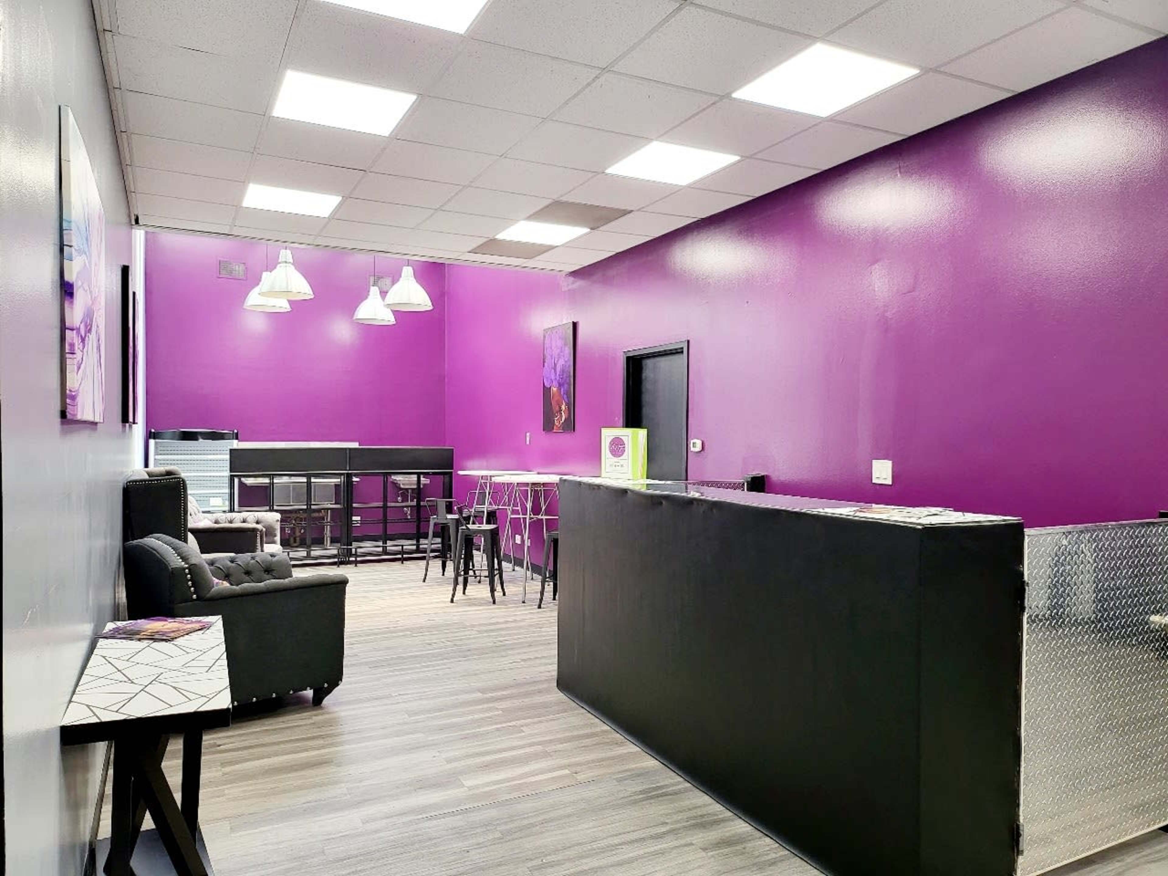 A brightly colored waiting area with purple walls, a reception desk, seating, and tables in a modern design.