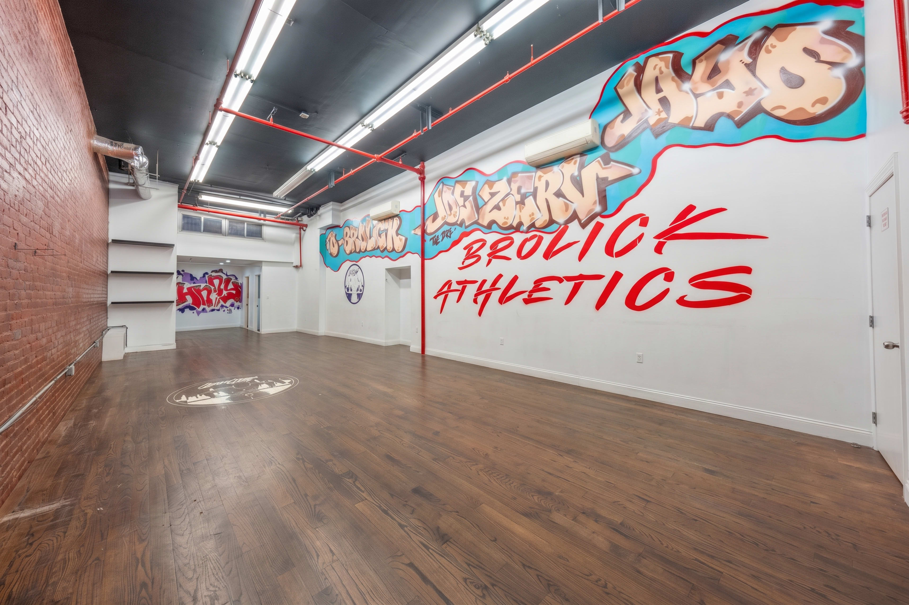 The image shows a spacious, empty indoor area with wooden flooring and walls decorated with colorful graffiti art.