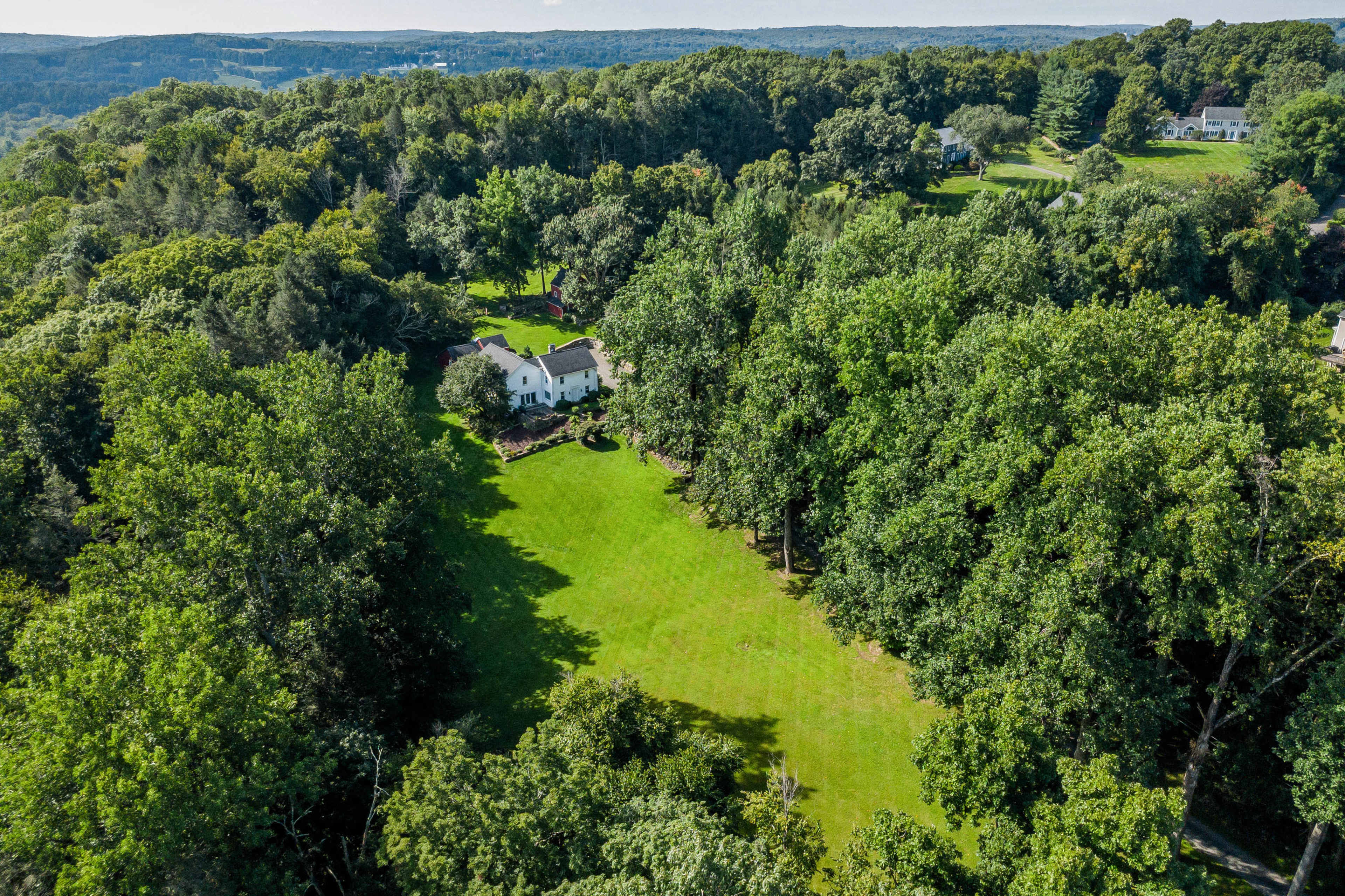 Aerial view of a large, green lawn surrounded by dense trees and a white house in the center.