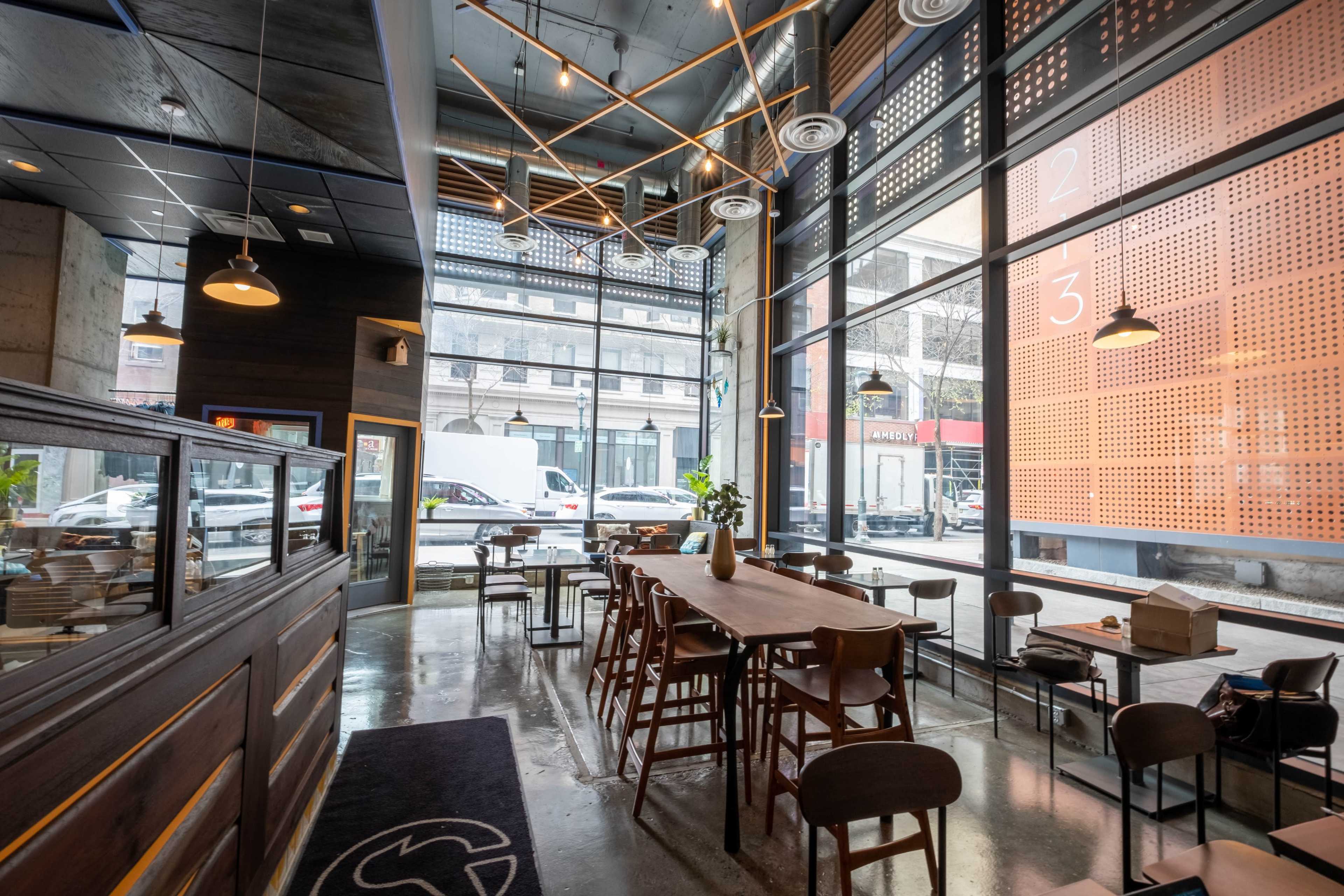 A modern café features large windows, wooden tables, and a minimalist interior design.