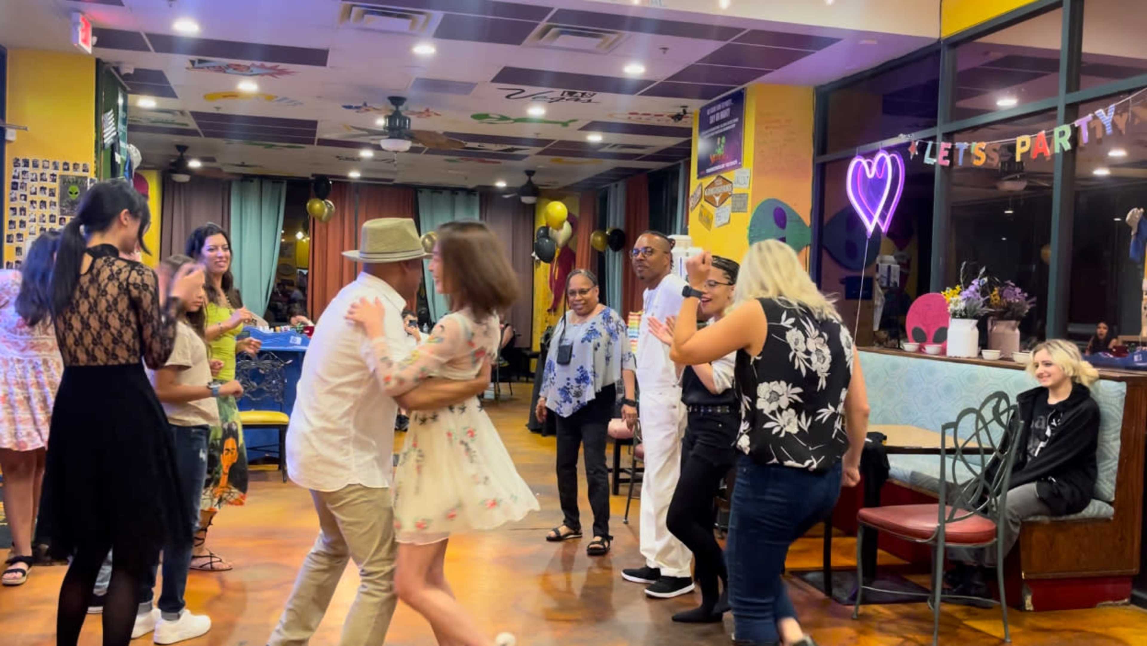 A group of people dance and socialize in a colorful venue decorated for a party.