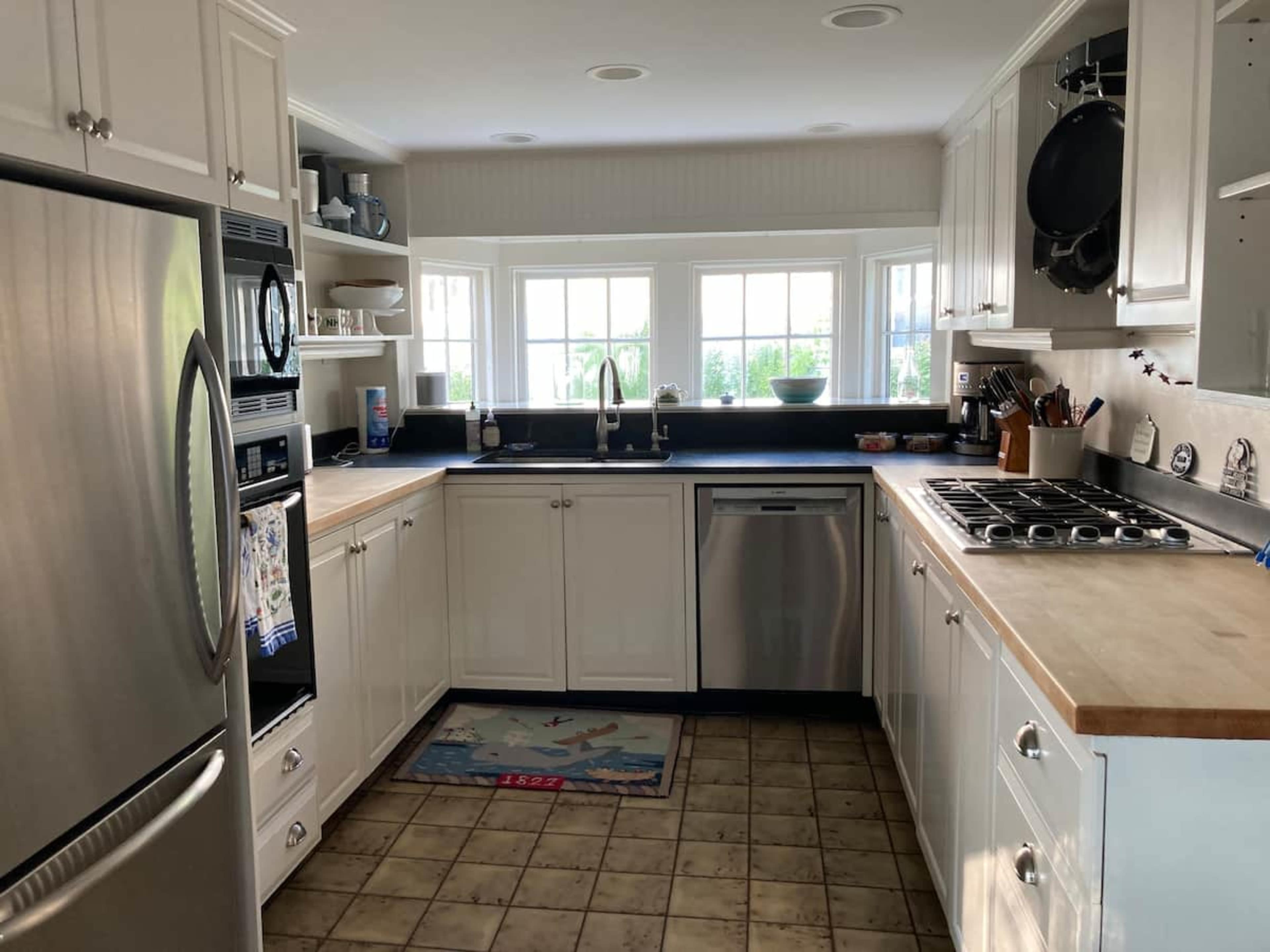 A modern kitchen with white cabinetry, a stainless steel refrigerator, and a countertop under a window with a view.