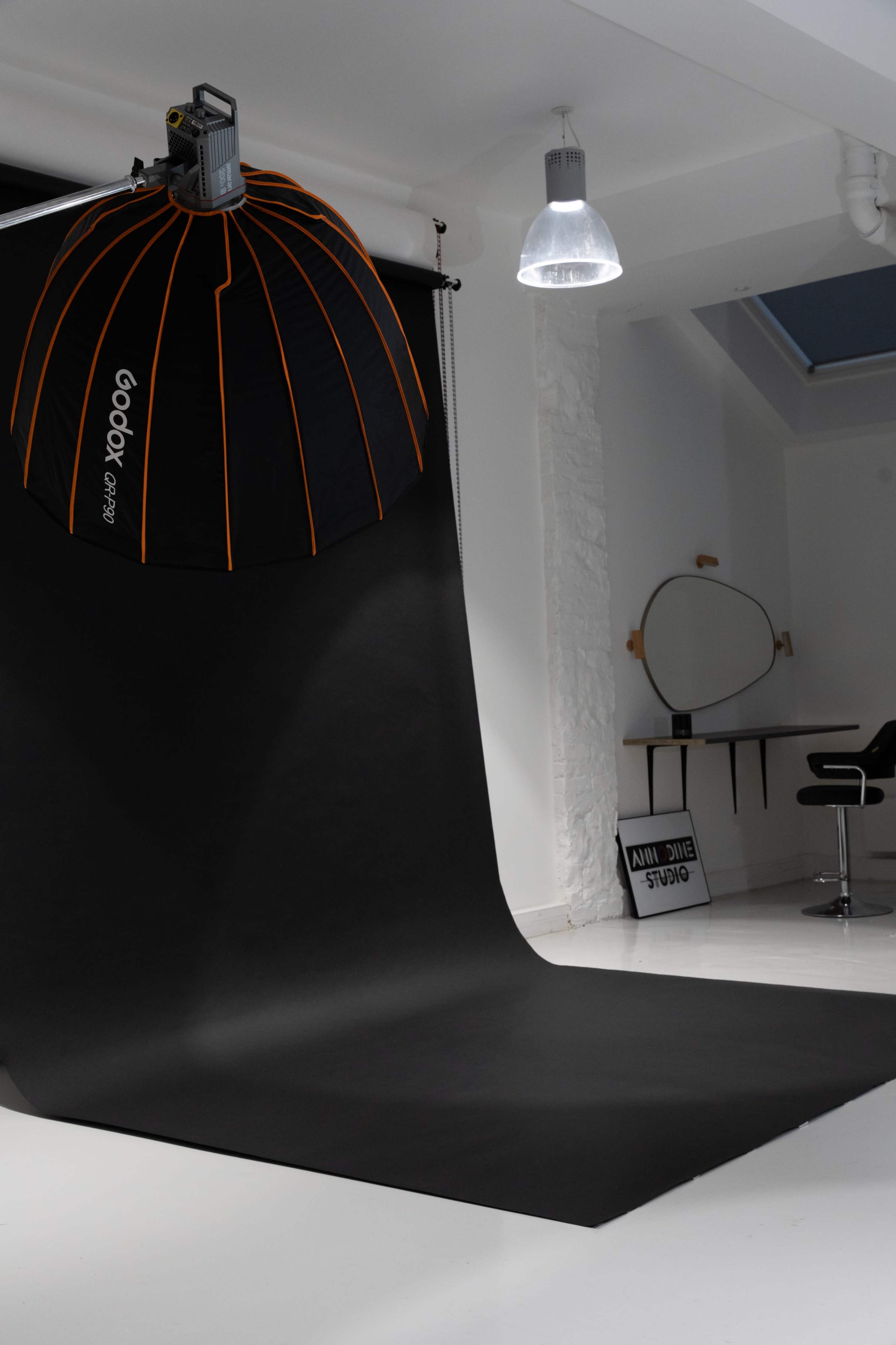 A photography studio featuring a large black backdrop and a softbox light setup.