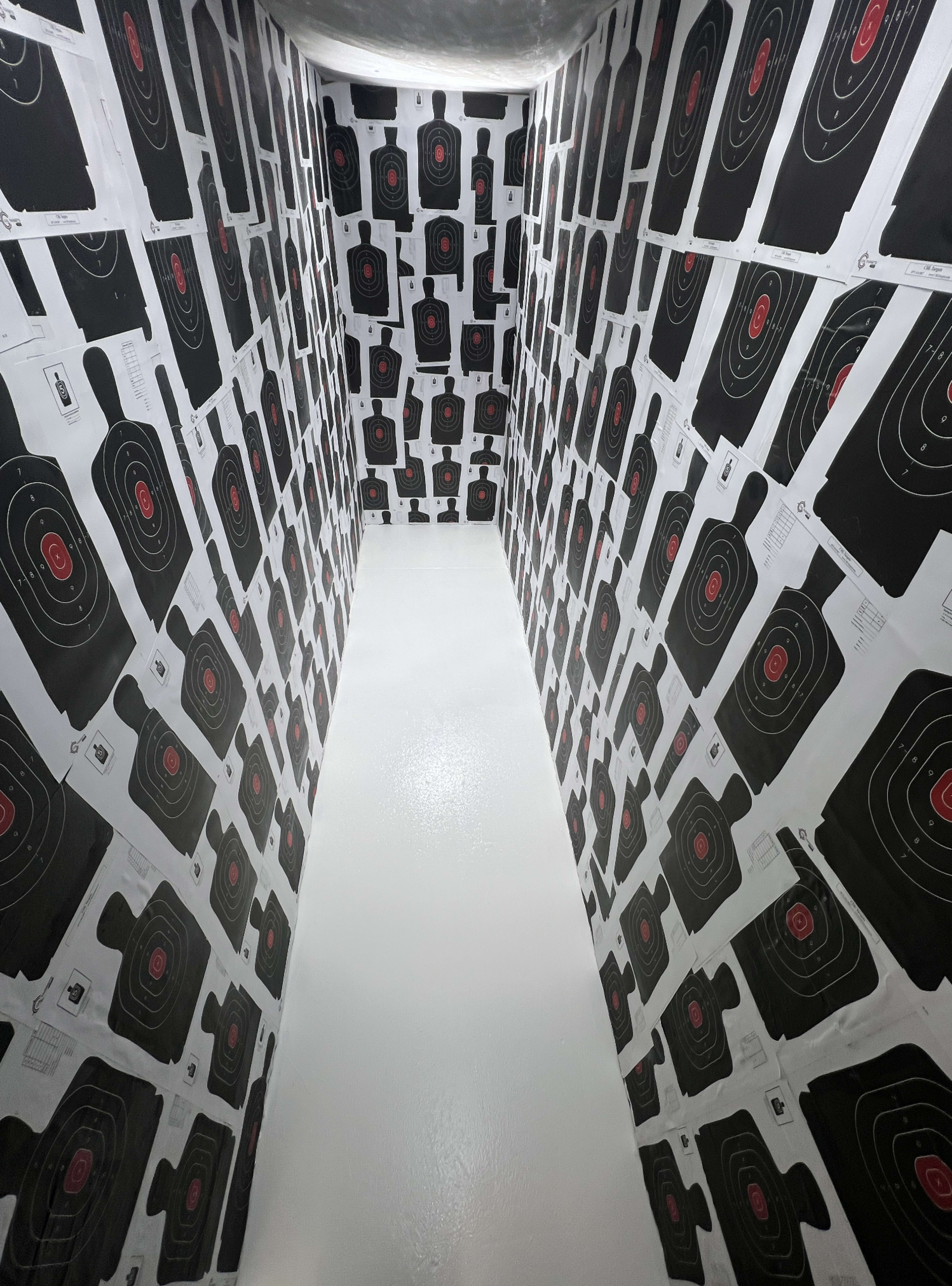 The image shows a narrow, enclosed space with walls covered in black and white target images featuring red bullseyes.