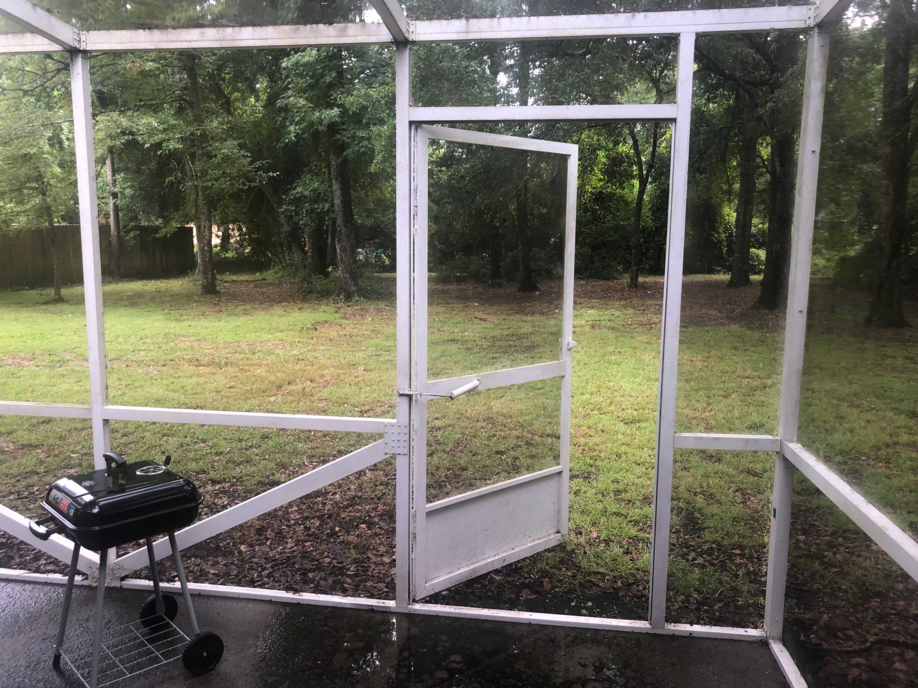 The image shows an open screen door leading to a grassy area with trees, alongside a small charcoal grill on the porch.