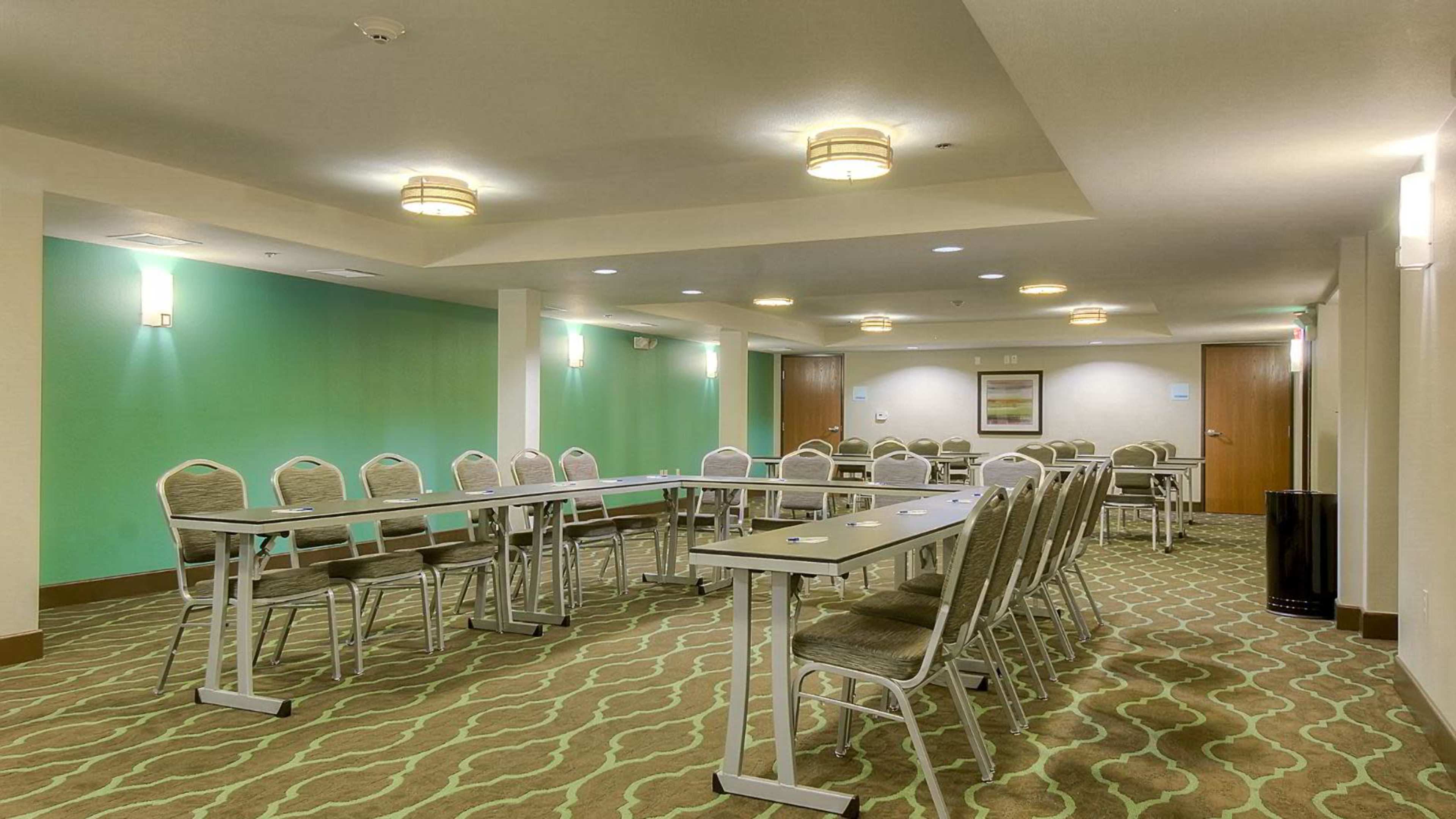 A conference room is set up with a series of tables and chairs arranged in a U-shape, featuring a green accent wall.