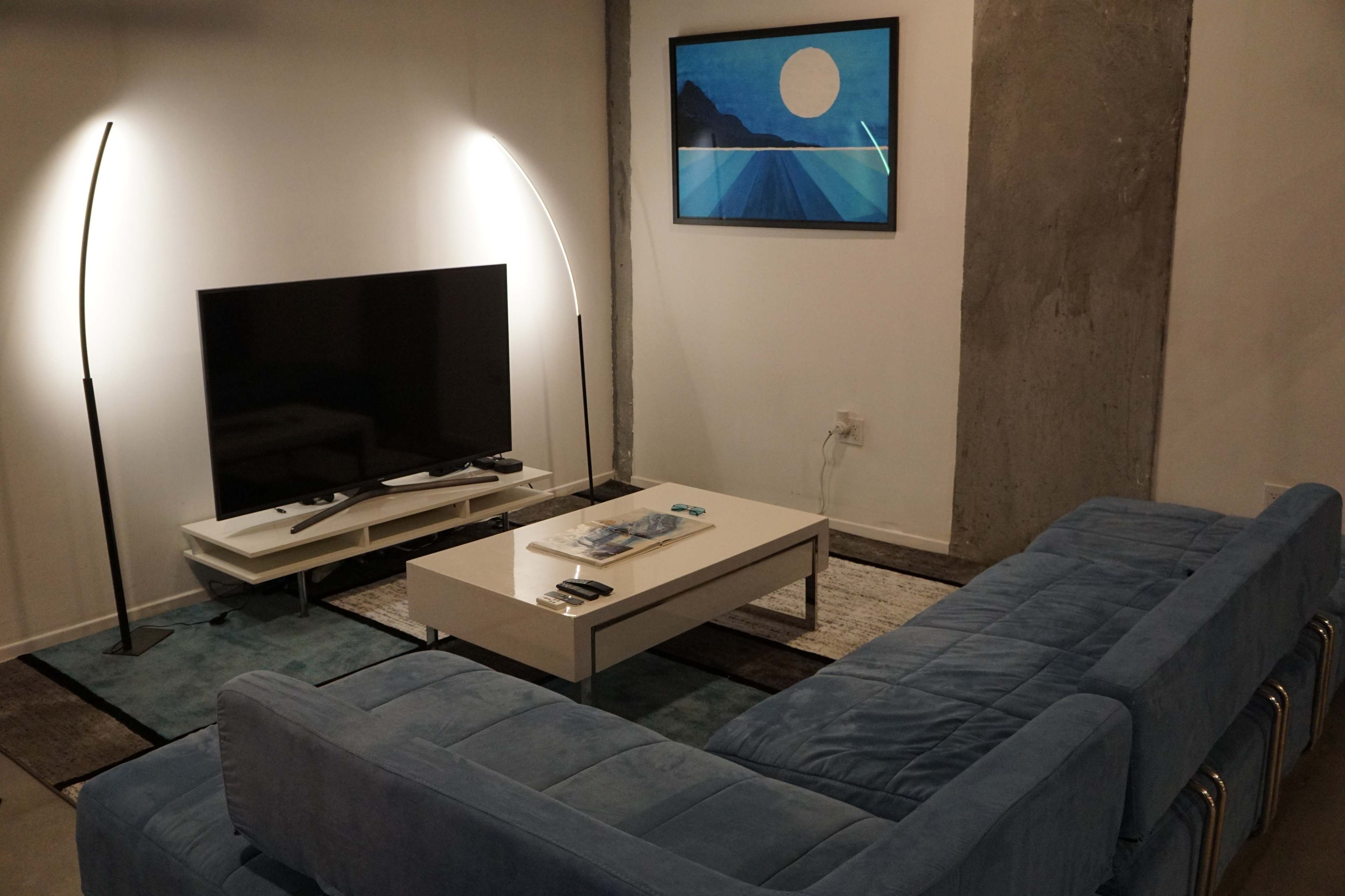 A modern living room featuring a blue sectional sofa, a coffee table, a television on a stand, and a large framed artwork on the wall.