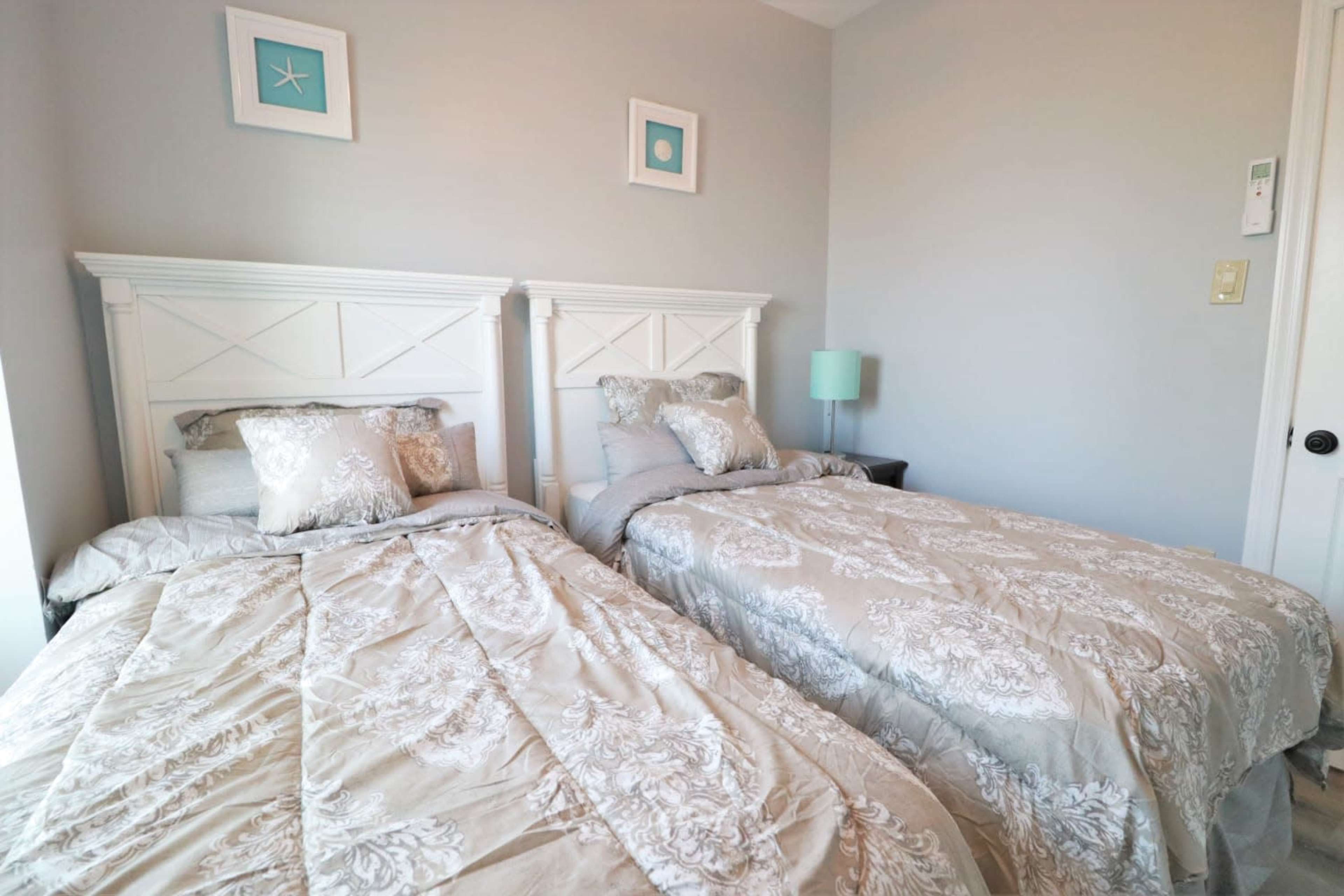 A small bedroom with two twin beds covered in gray and white bedding, framed by light-colored walls and decor.