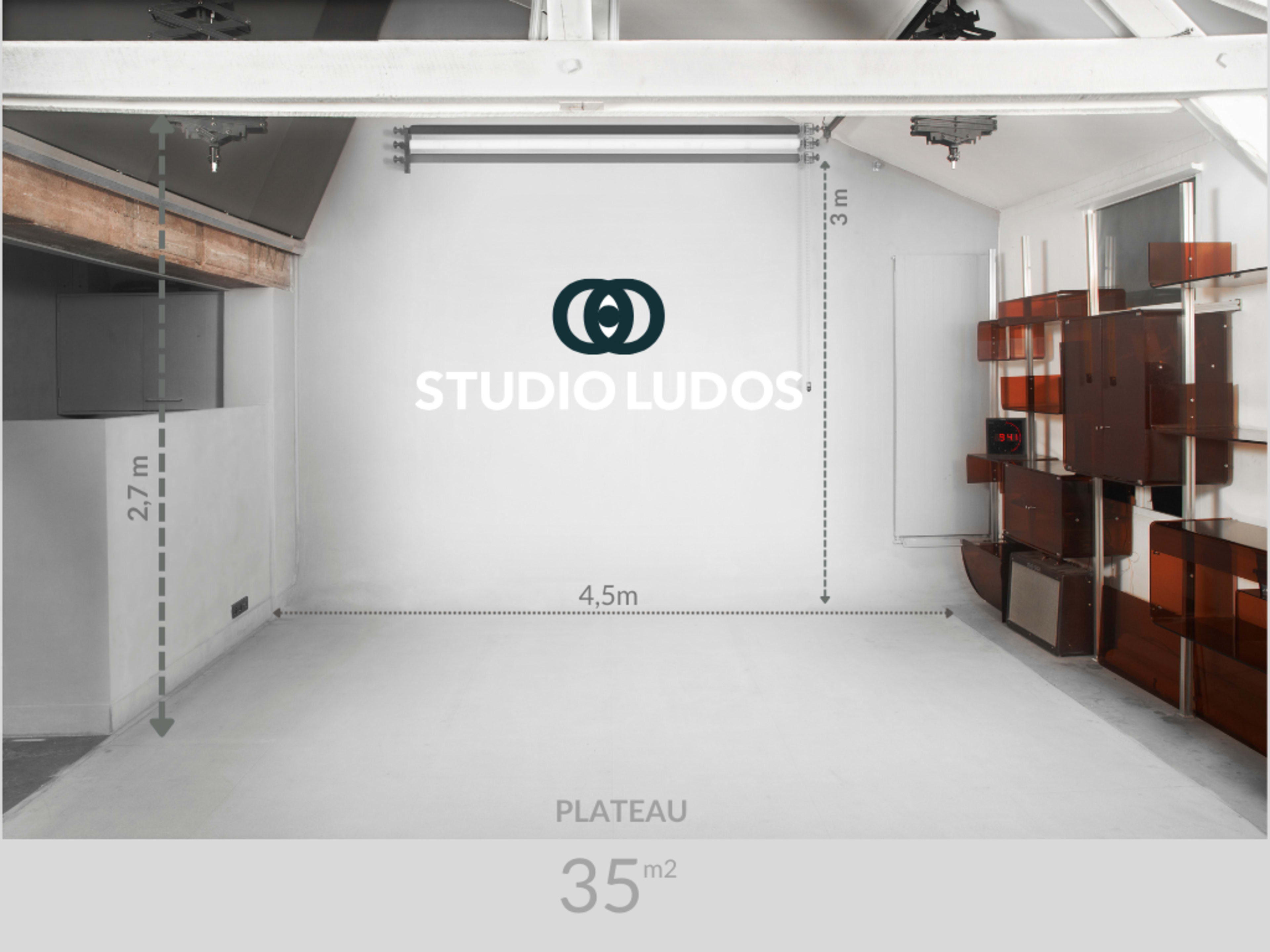 The image shows a spacious studio with a high ceiling, featuring a large logo on the wall and various storage units along one side.