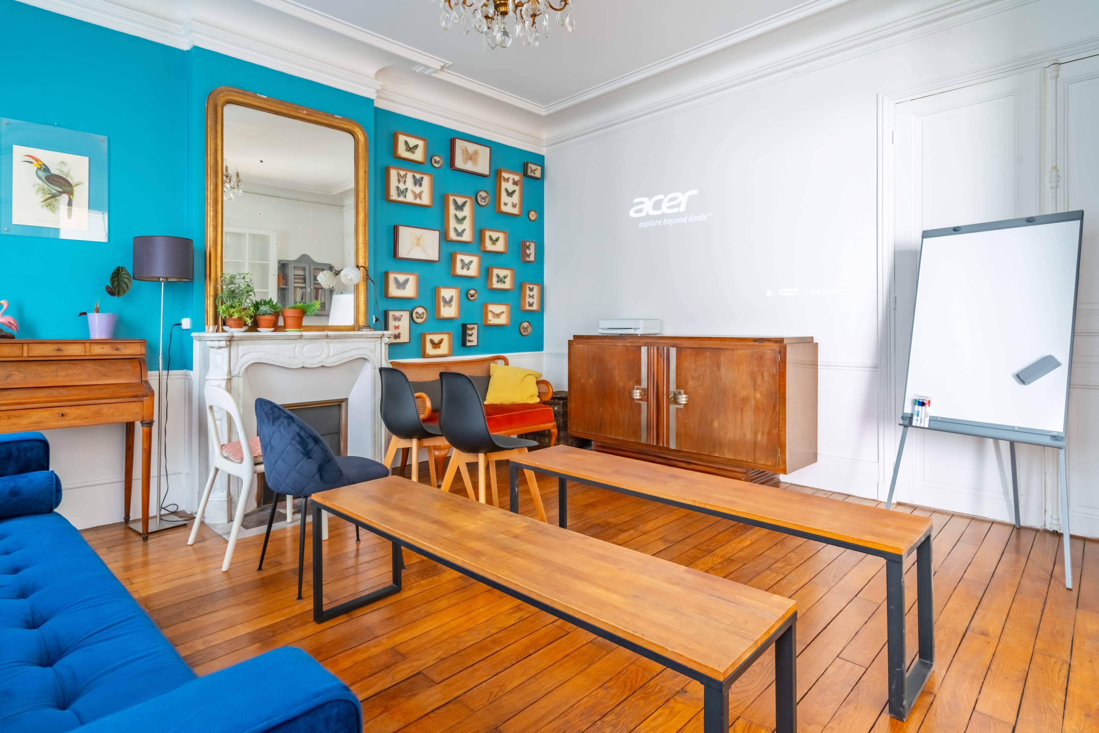 A brightly colored room features a wooden table, benches, a projector displaying "acer," and various framed art pieces on the walls.