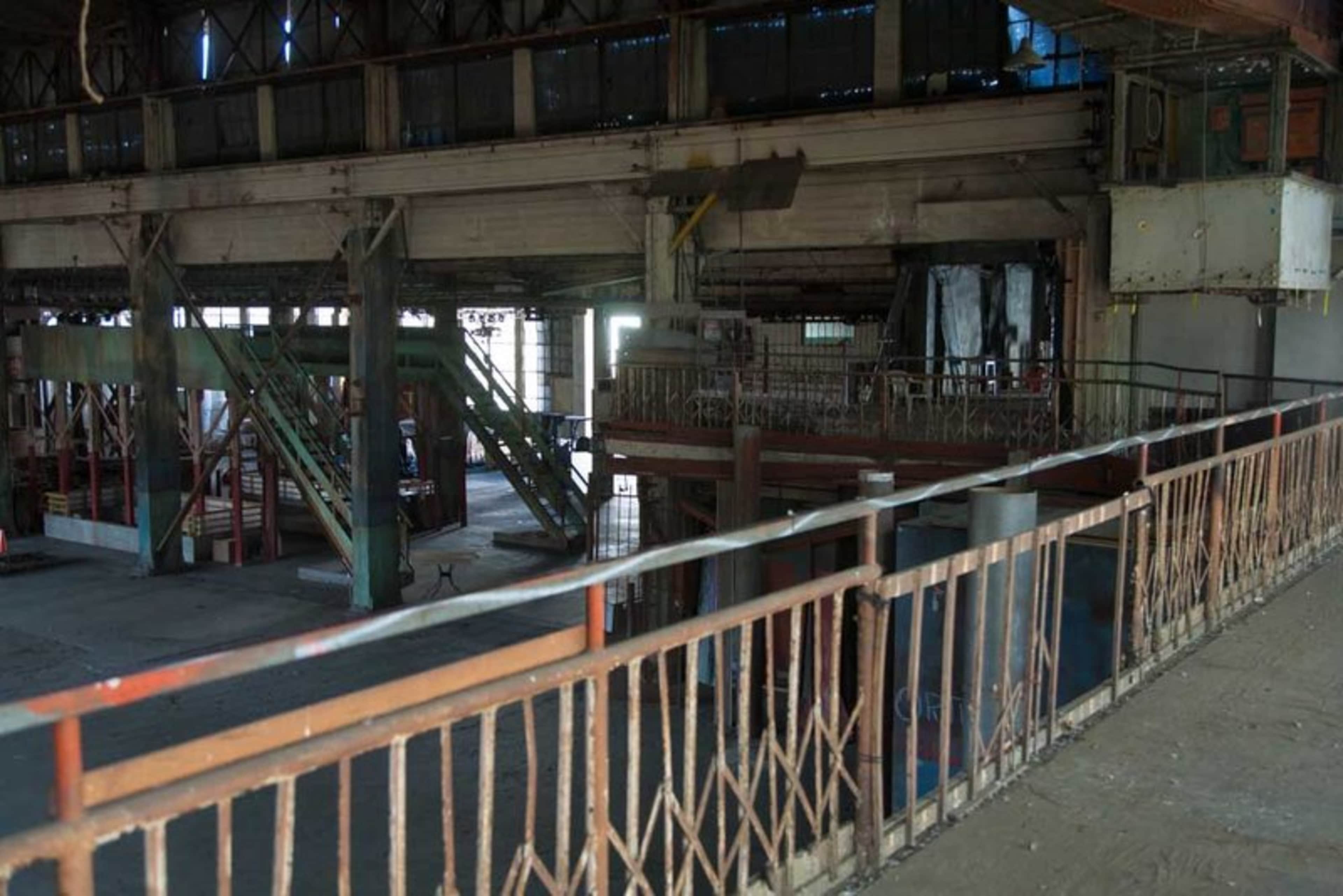 An industrial interior with exposed metal beams, a staircase, and various machinery in an abandoned state.