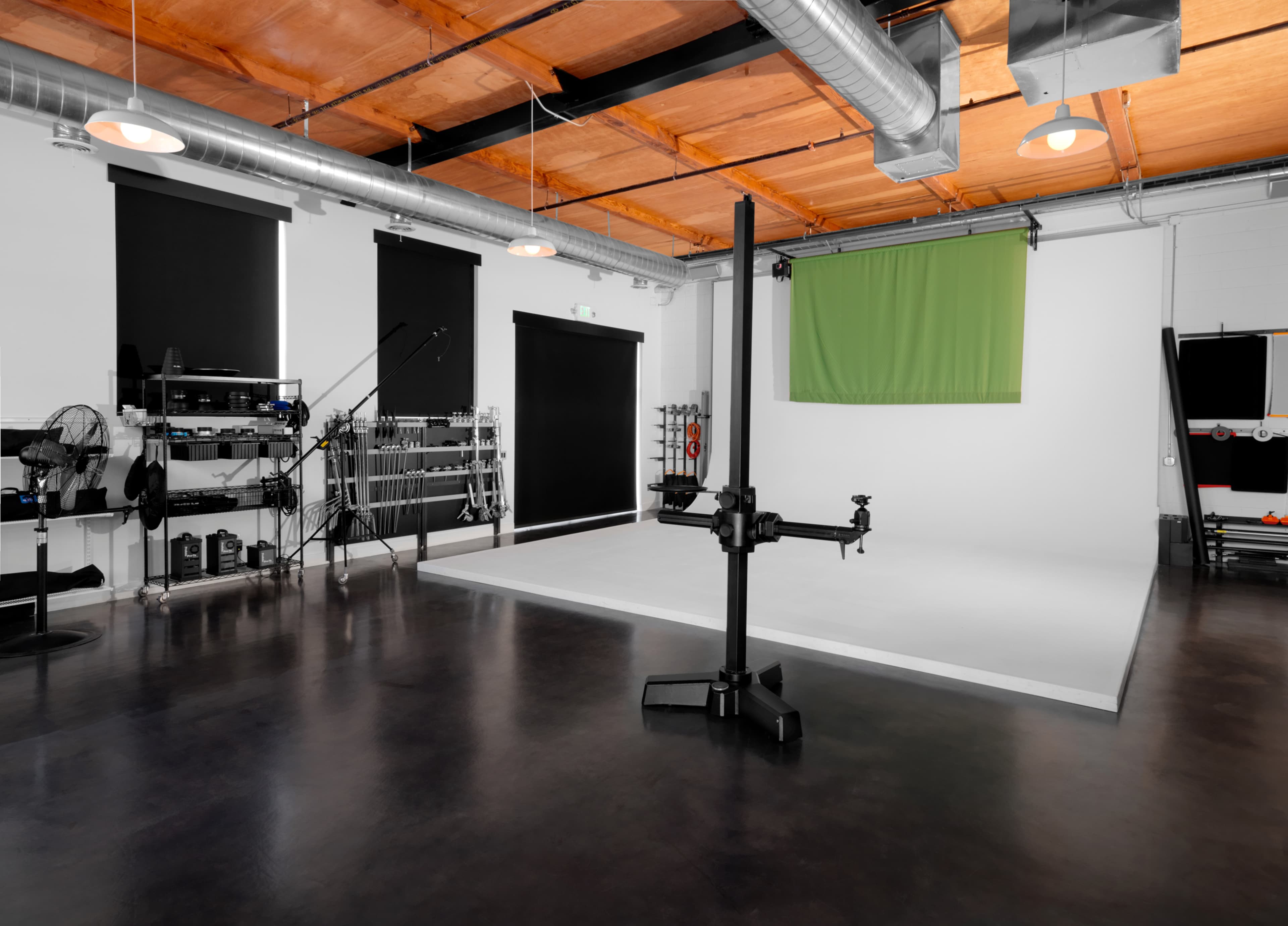 A spacious photography studio with a white backdrop, green screen, and various equipment arranged along the walls.