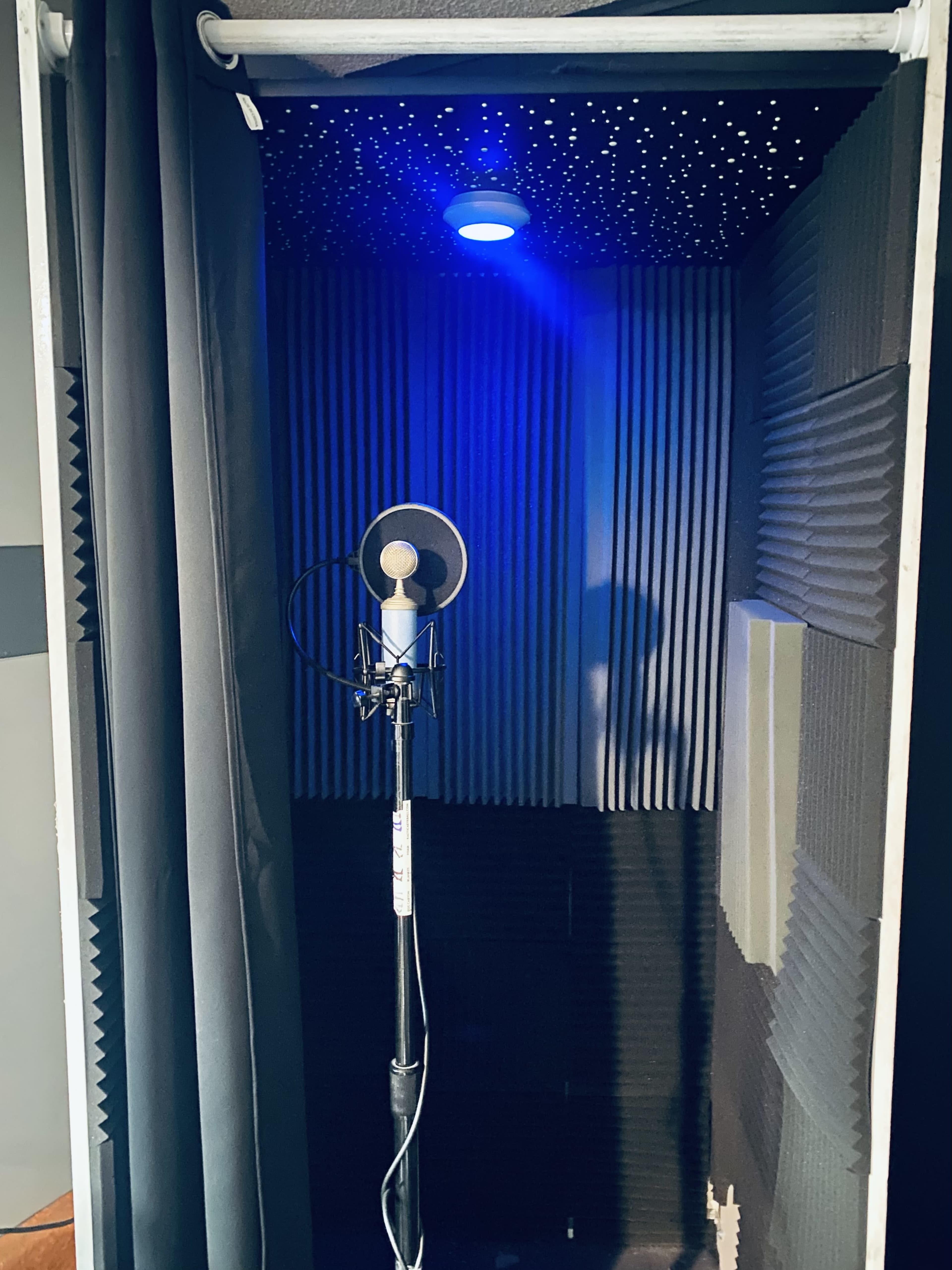 A soundproof recording booth with a microphone on a stand and dark curtains.