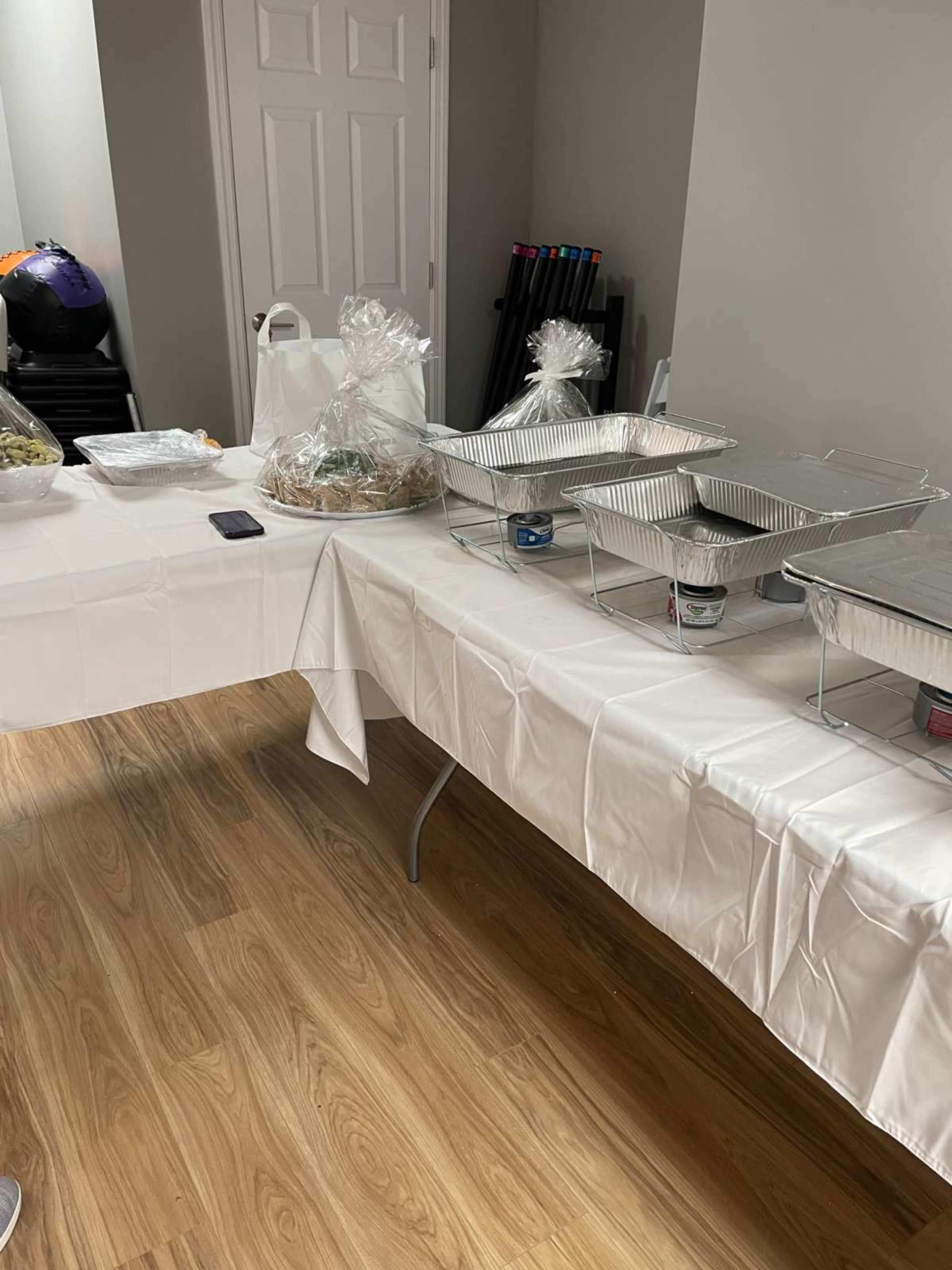 A table covered with a white tablecloth displays various food containers, including aluminum trays and a gift bag.