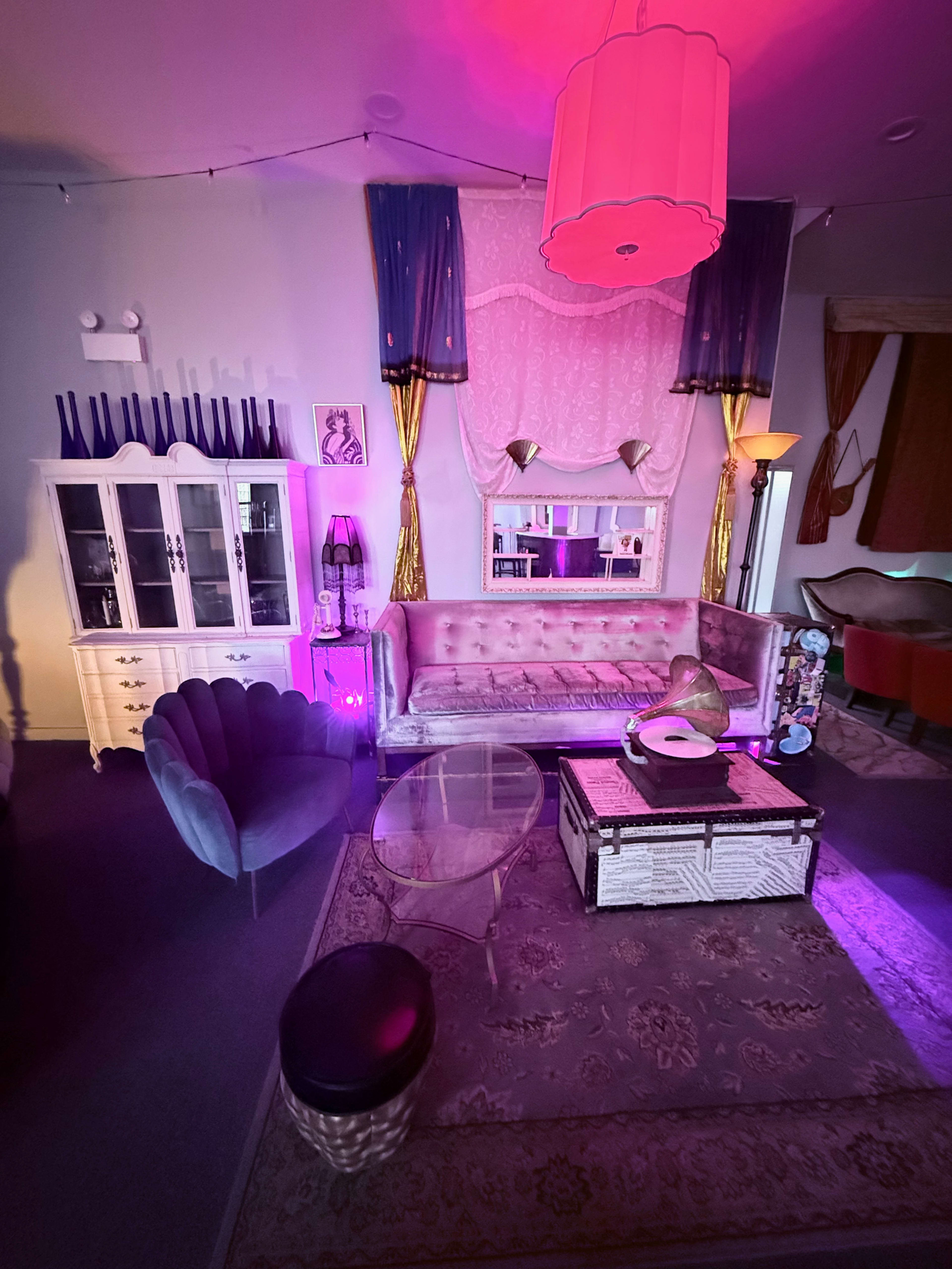 The image shows a brightly lit vintage-style living room with a plush sofa, a glass coffee table, and various decorative elements.