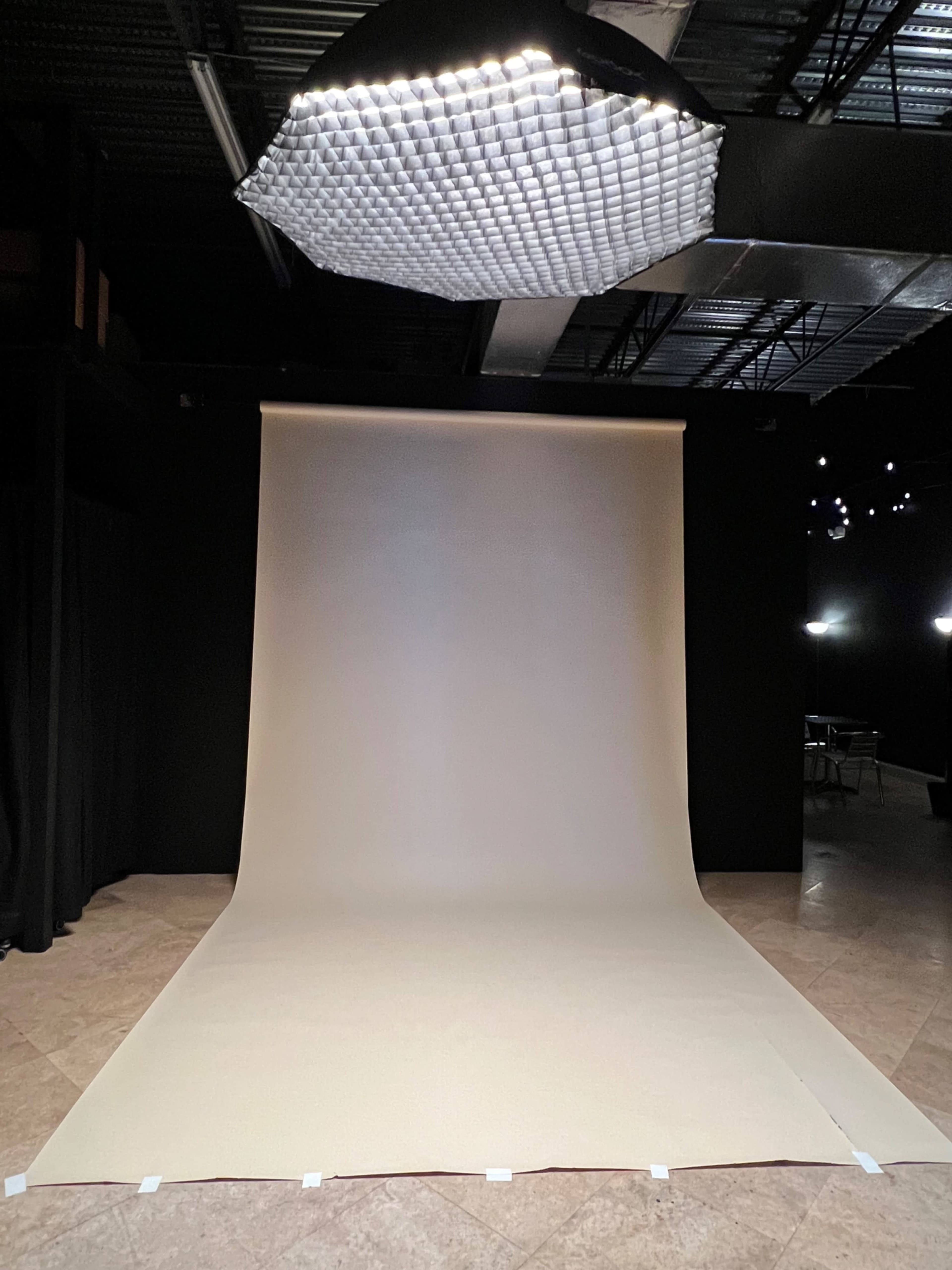 A photography studio with a beige backdrop and a grid light fixture overhead.