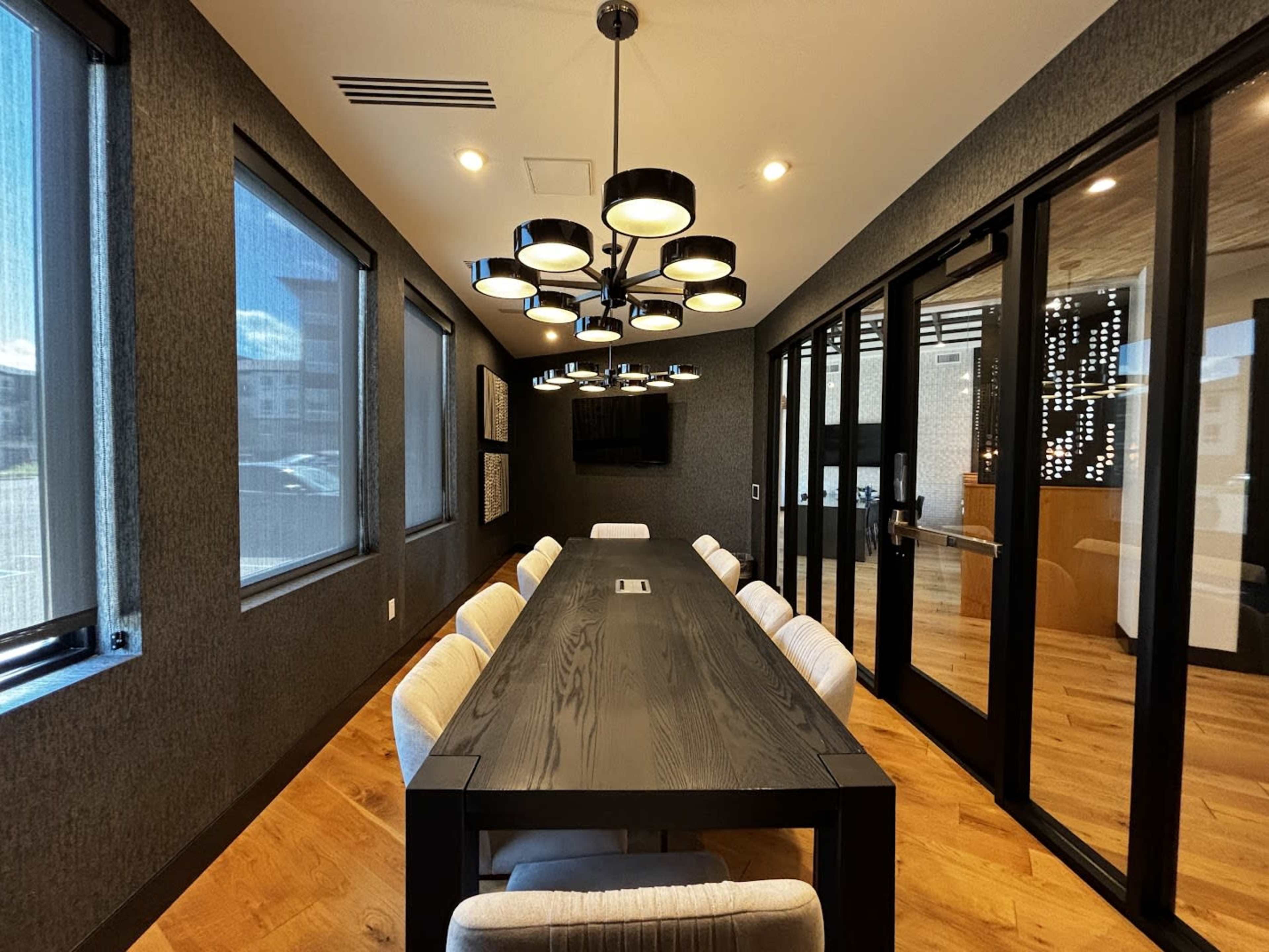 The image shows a modern conference room featuring a long black table surrounded by upholstered chairs and a distinctive light fixture.
