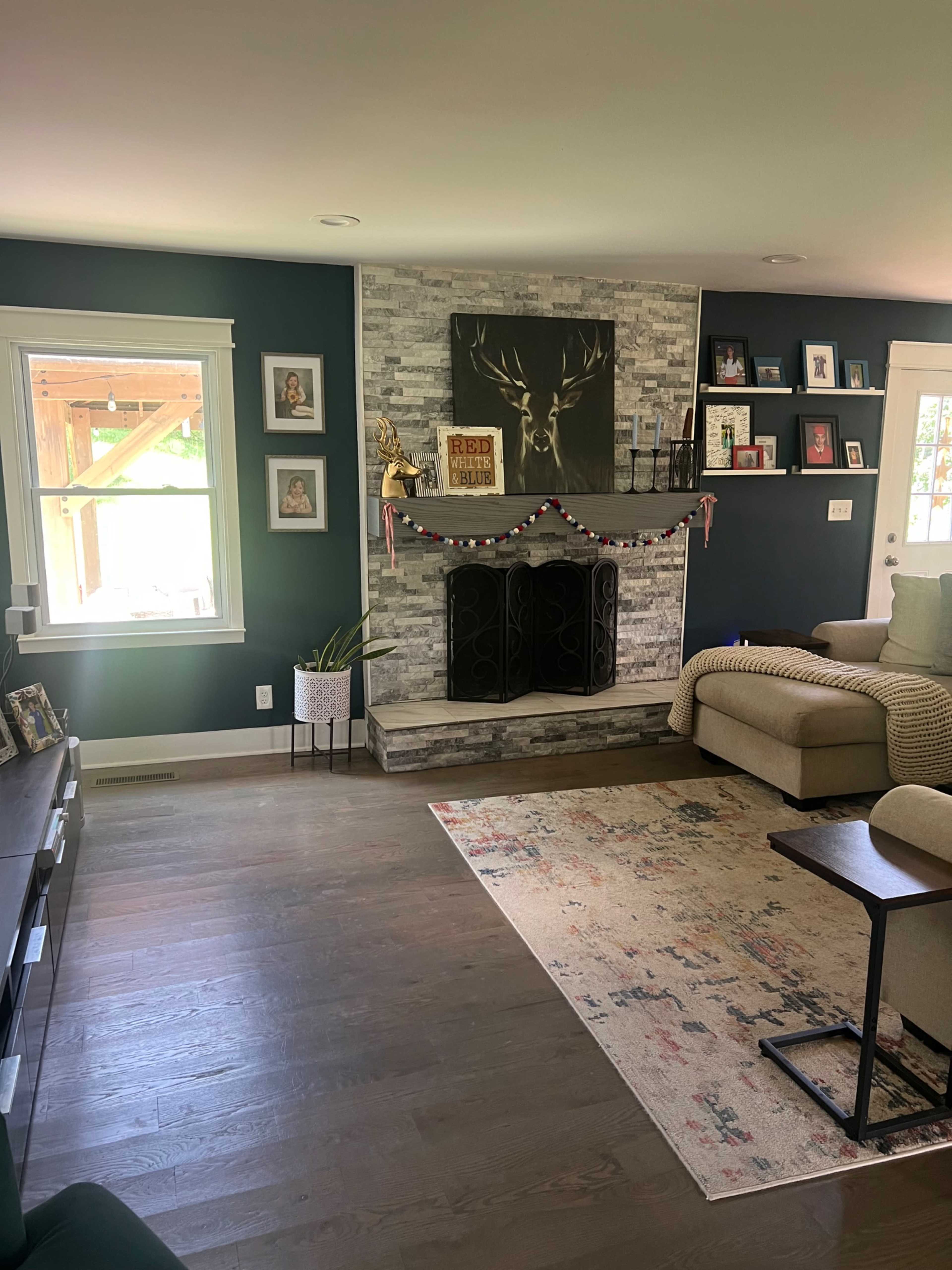 The image shows a living room with a stone fireplace, framed photos on the walls, a couch, and a small table beside it.