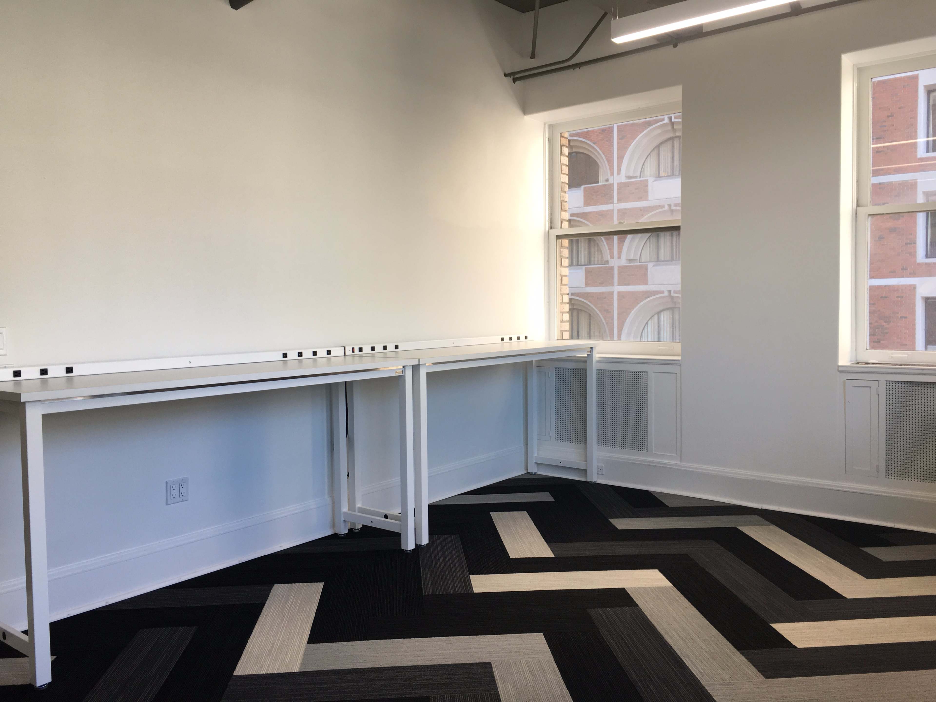 A bright, minimalist room with two white tables against a wall and a patterned black and gray carpet.