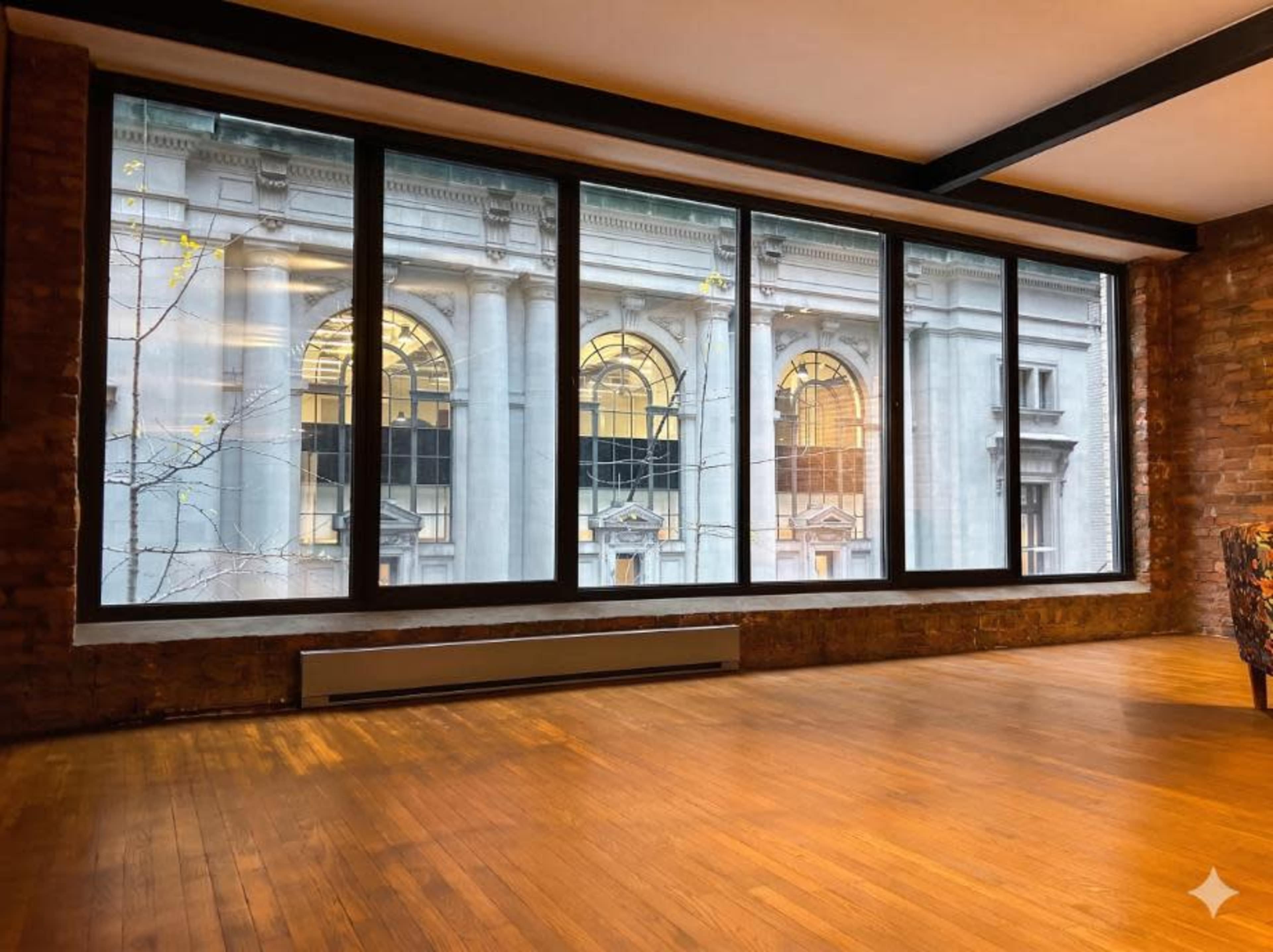 The image shows a spacious interior room with large windows offering a view of a historic building across the street.