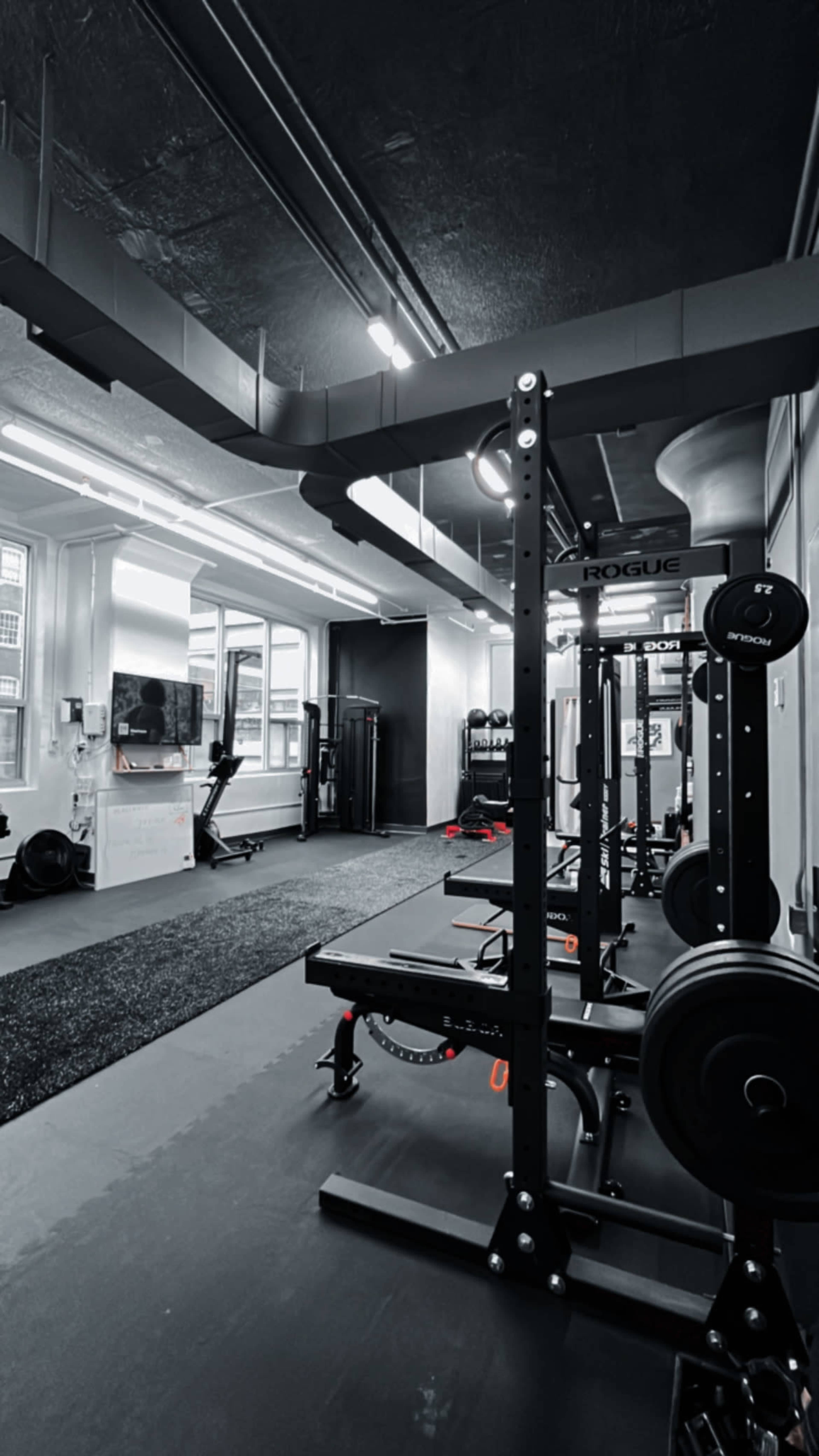 A modern gym interior with weightlifting equipment, including a squat rack and a treadmill, under bright overhead lighting.