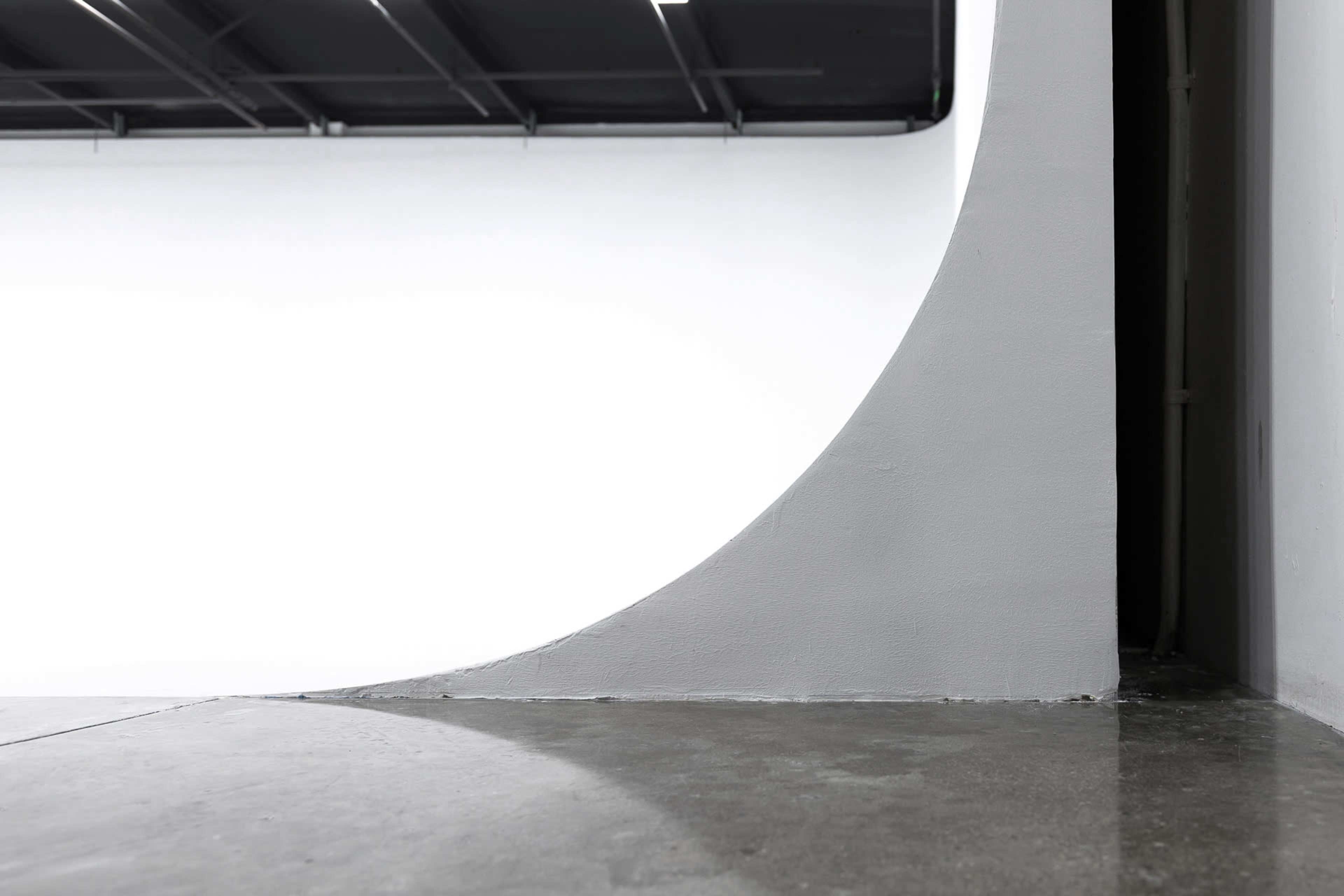 A minimalist interior with a curved gray wall meeting a smooth concrete floor and a white background.