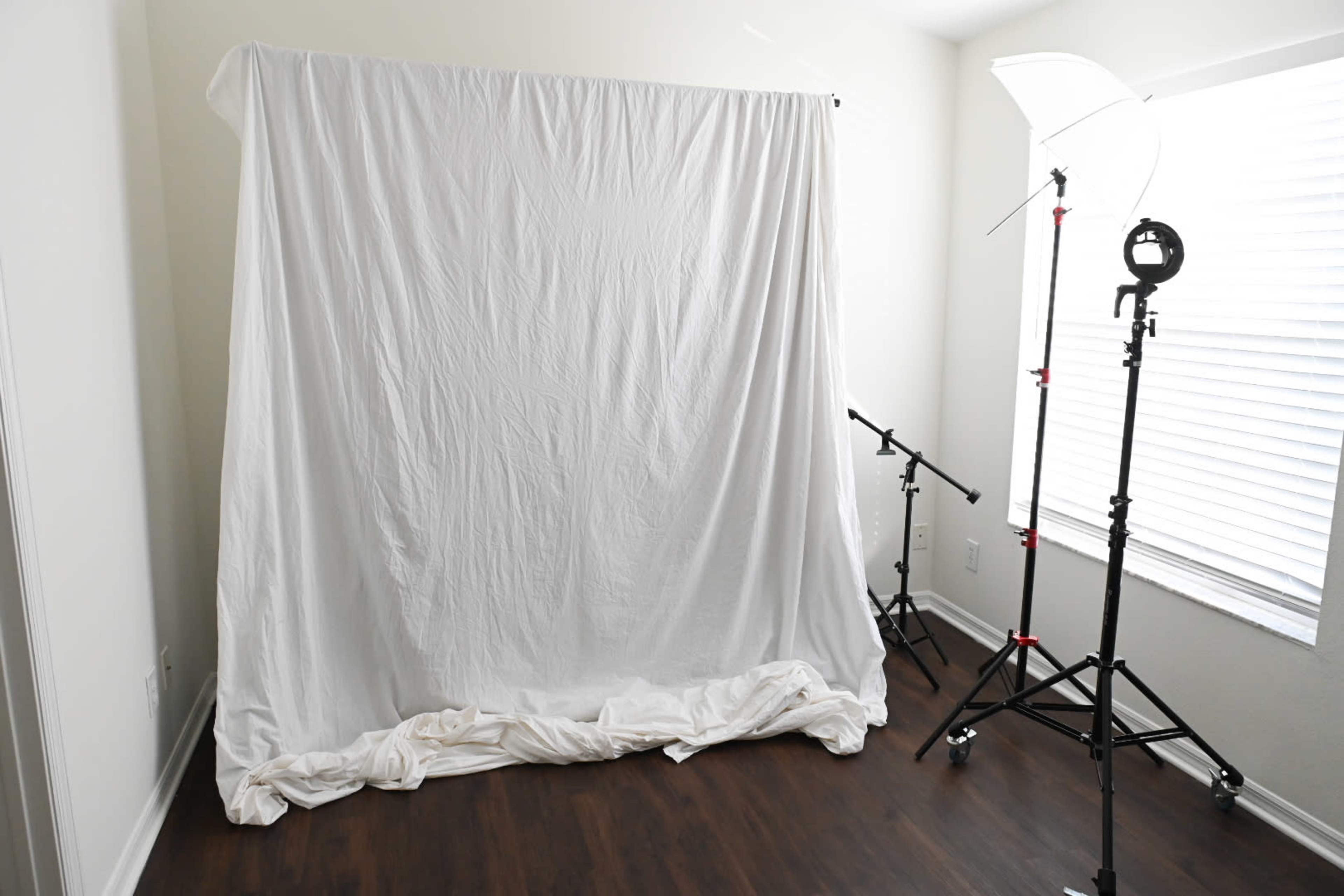The image shows a simple photography setup with a wrinkled white backdrop and lighting equipment positioned in a room with a window.