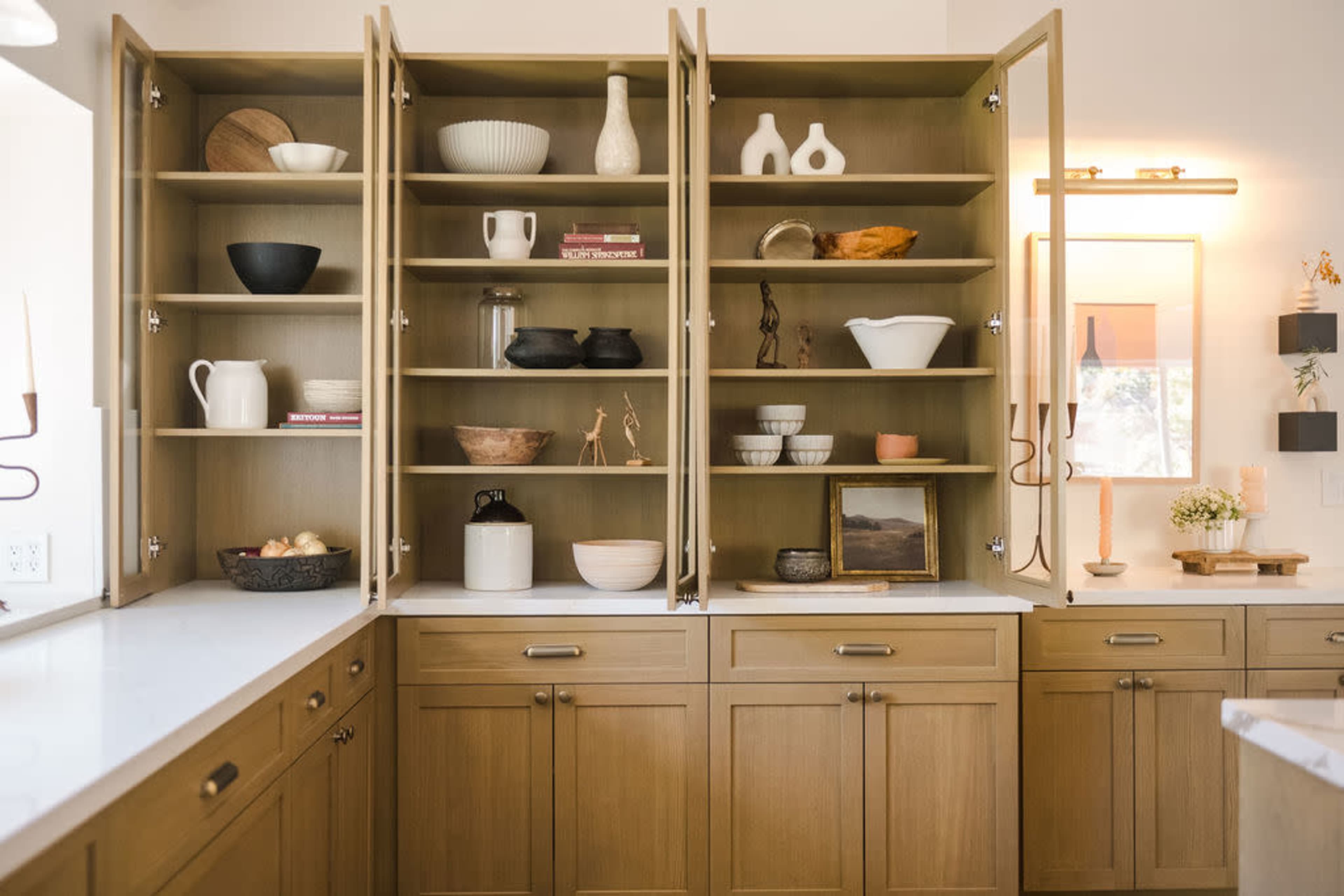 A well-organized kitchen cabinet with open shelves displaying various decorative items and dishware in a modern design.