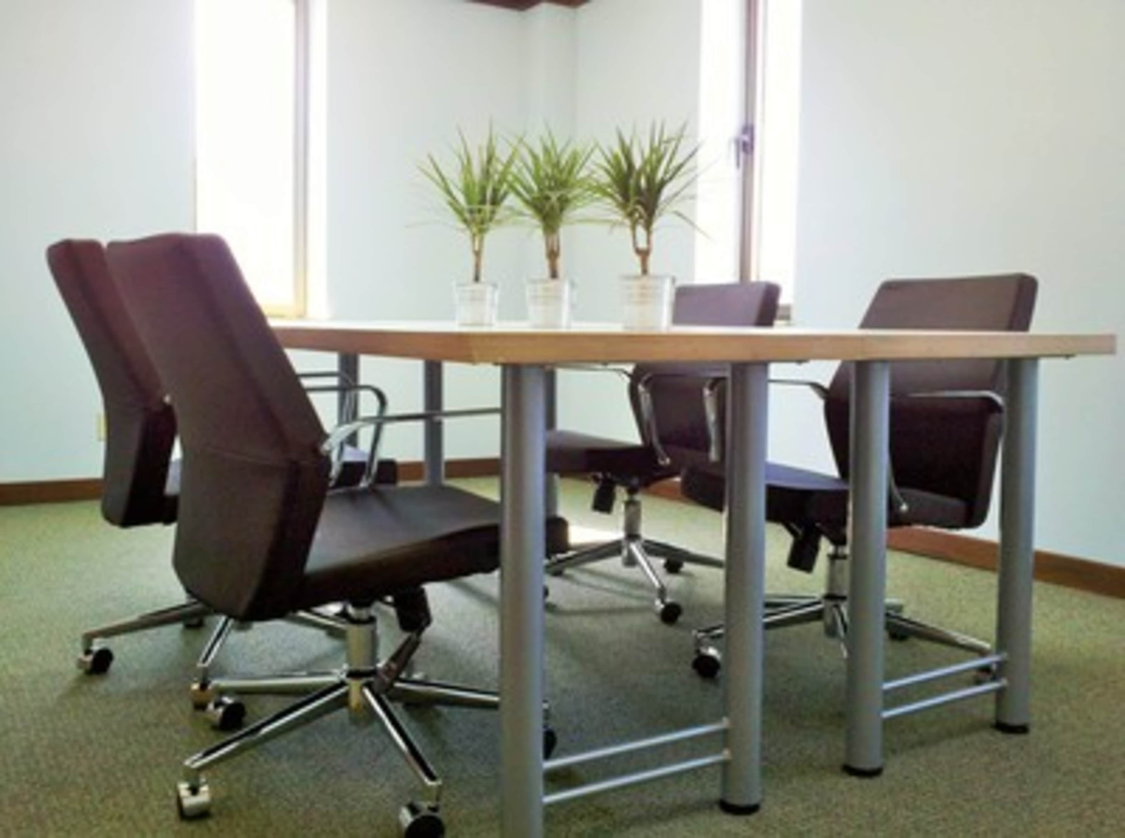 A modern conference room features a table surrounded by four rolling chairs and two small potted plants on the table.