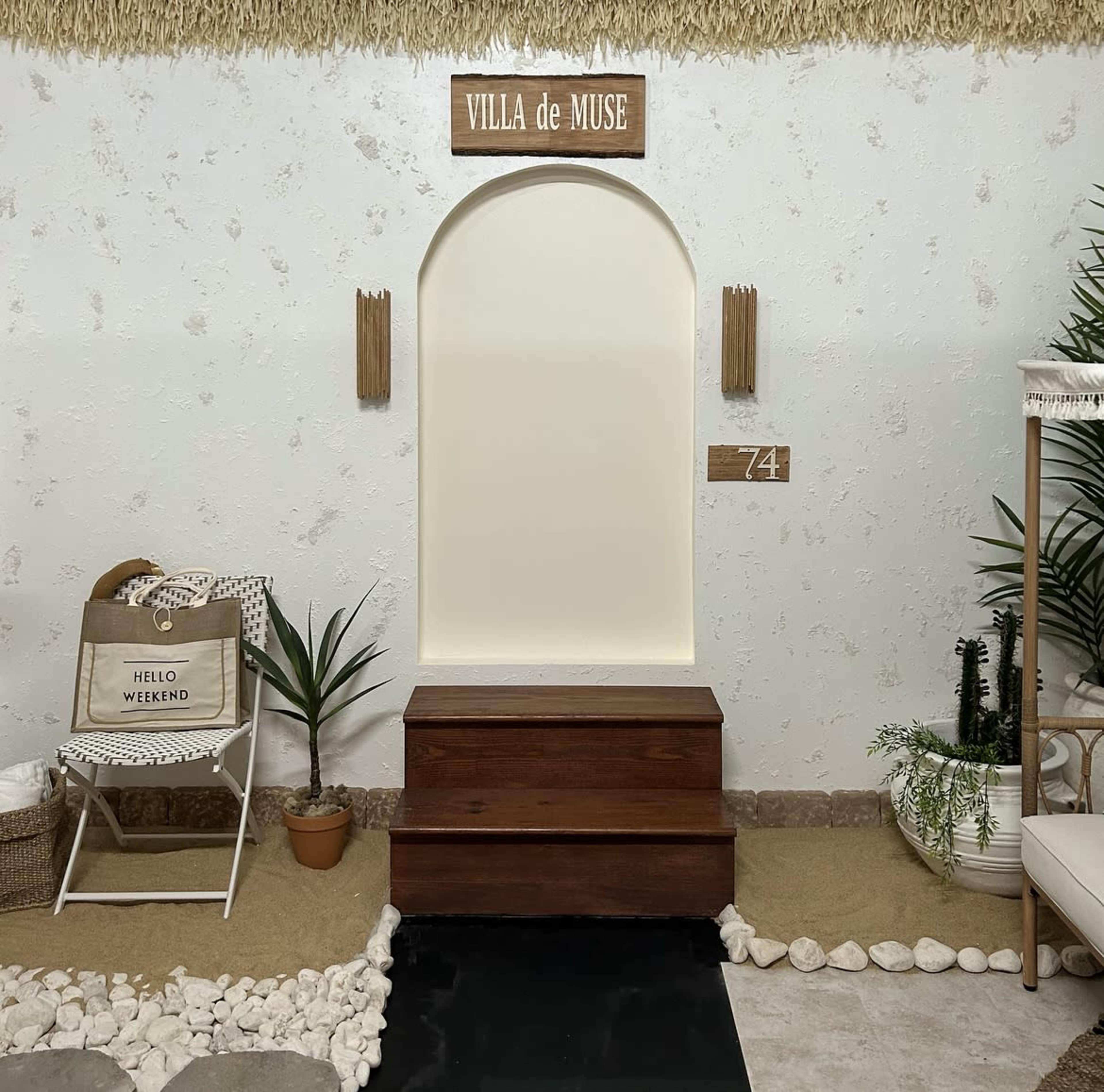 A minimalist interior space featuring a wooden chest, a decorative arch, and elements such as a plant, a chair, and a sign reading "VILLA de MUSE."