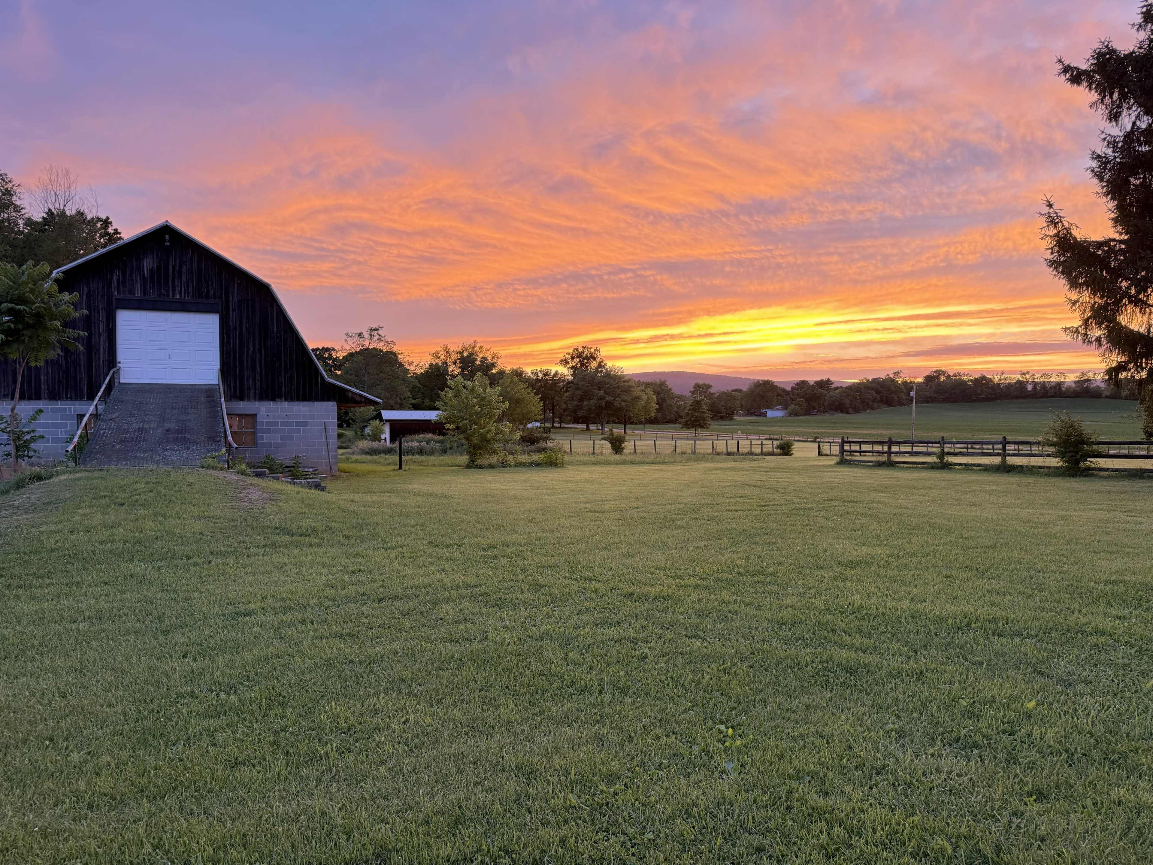A barn stands on a grassy field under a vibrant sunset with colorful clouds.