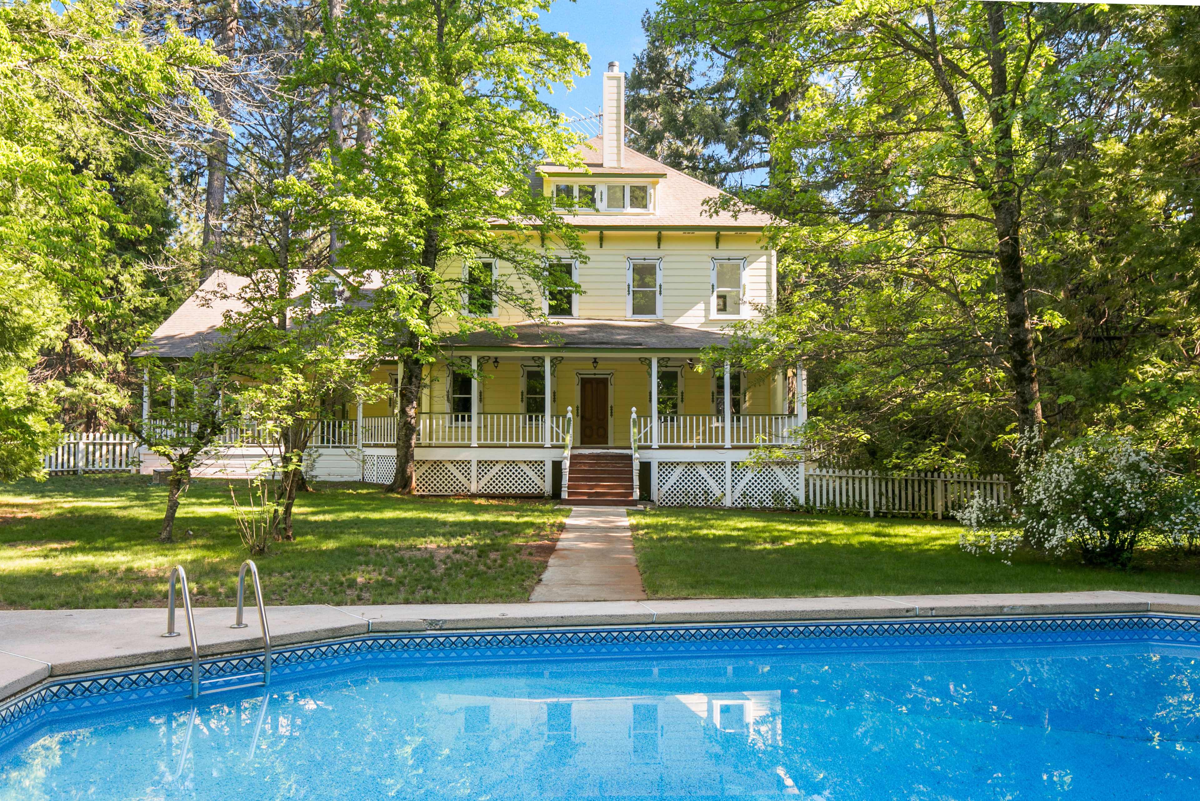A large, two-story yellow house with a porch and surrounded by trees is visible behind a swimming pool.