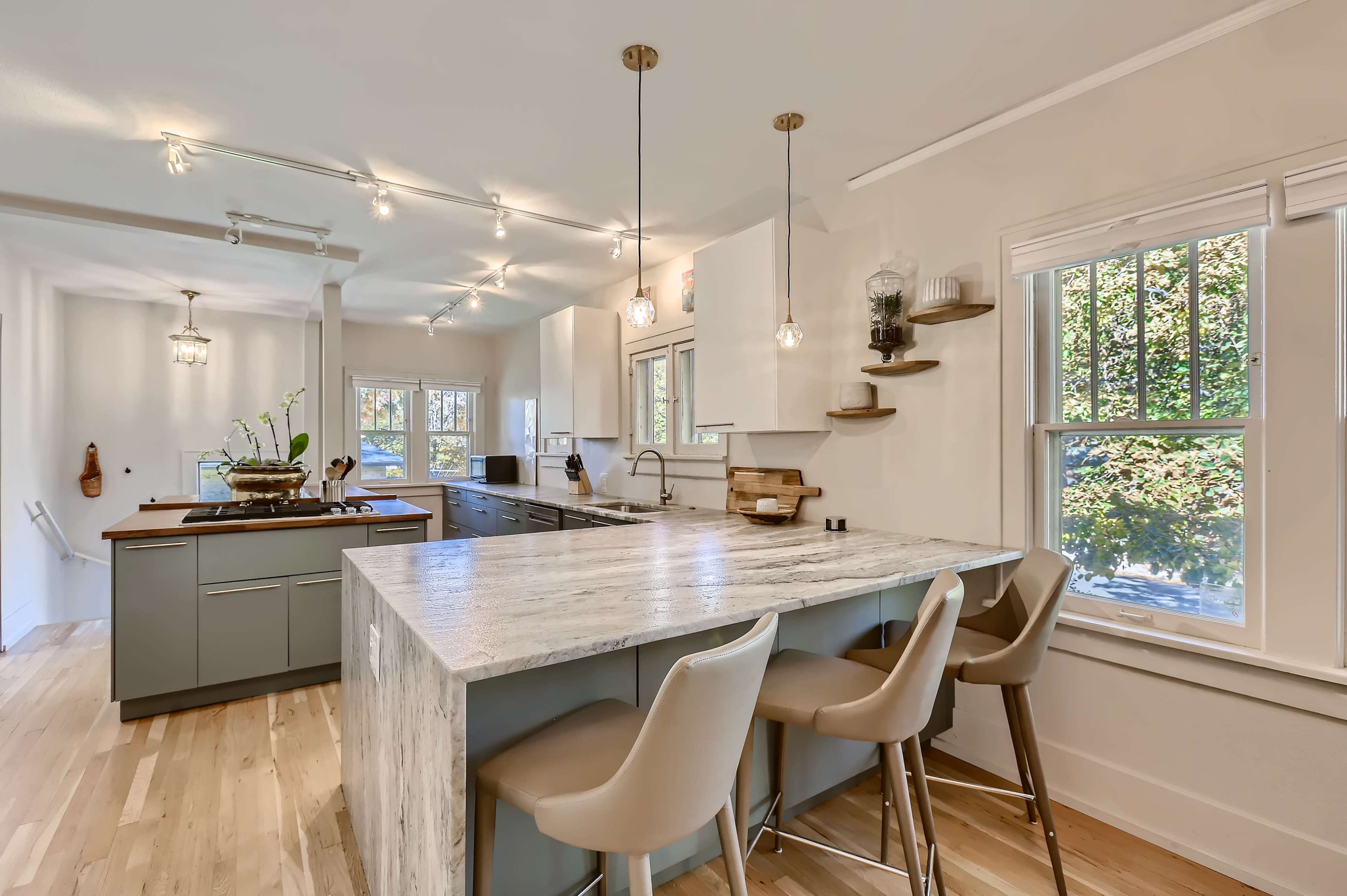 A modern kitchen features a large island with a marble countertop, bar stools, and stylish lighting.